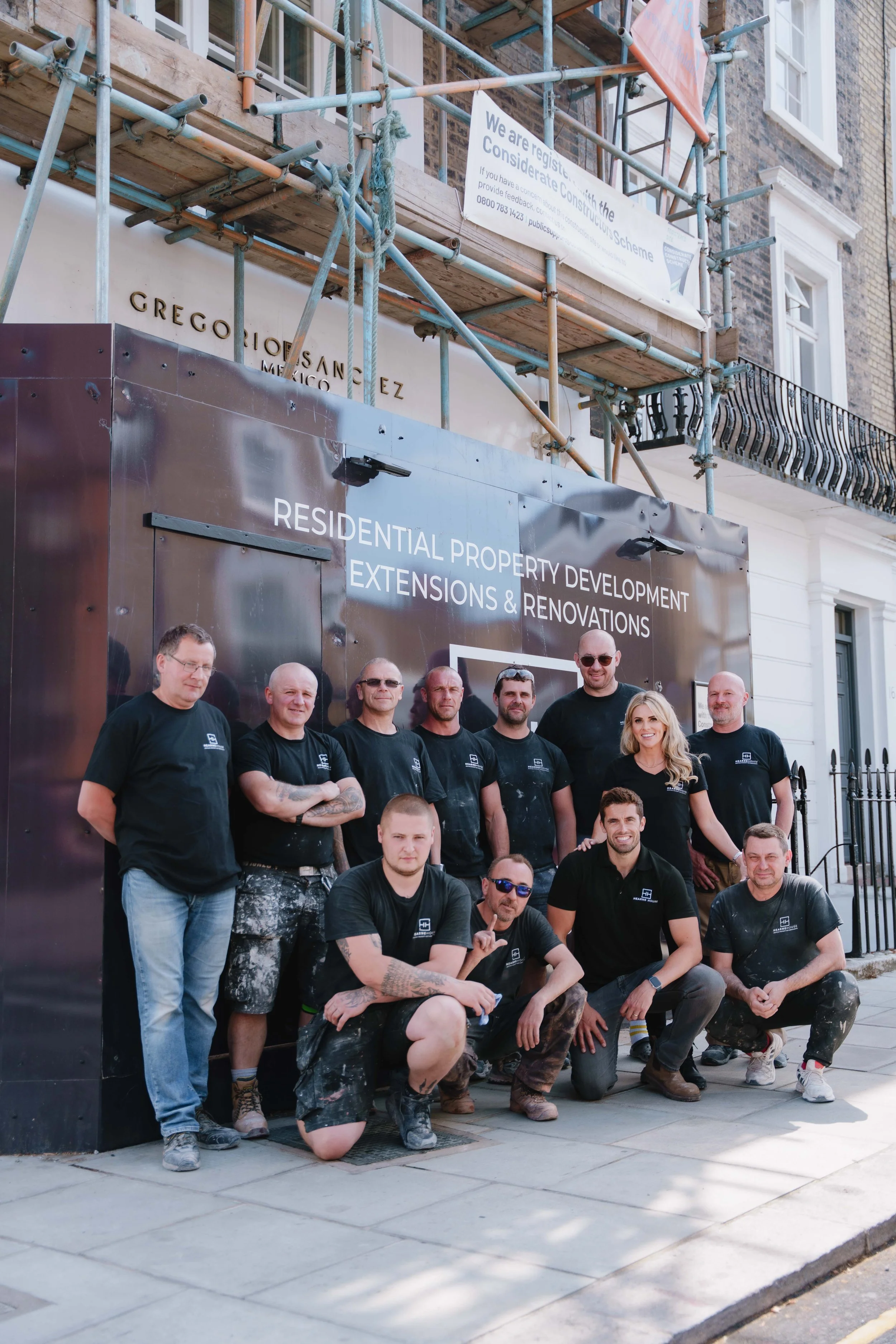 Group of construction workers posing in front of a building with scaffolding and a sign that reads "Residential Property Development, Extensions & Renovations".