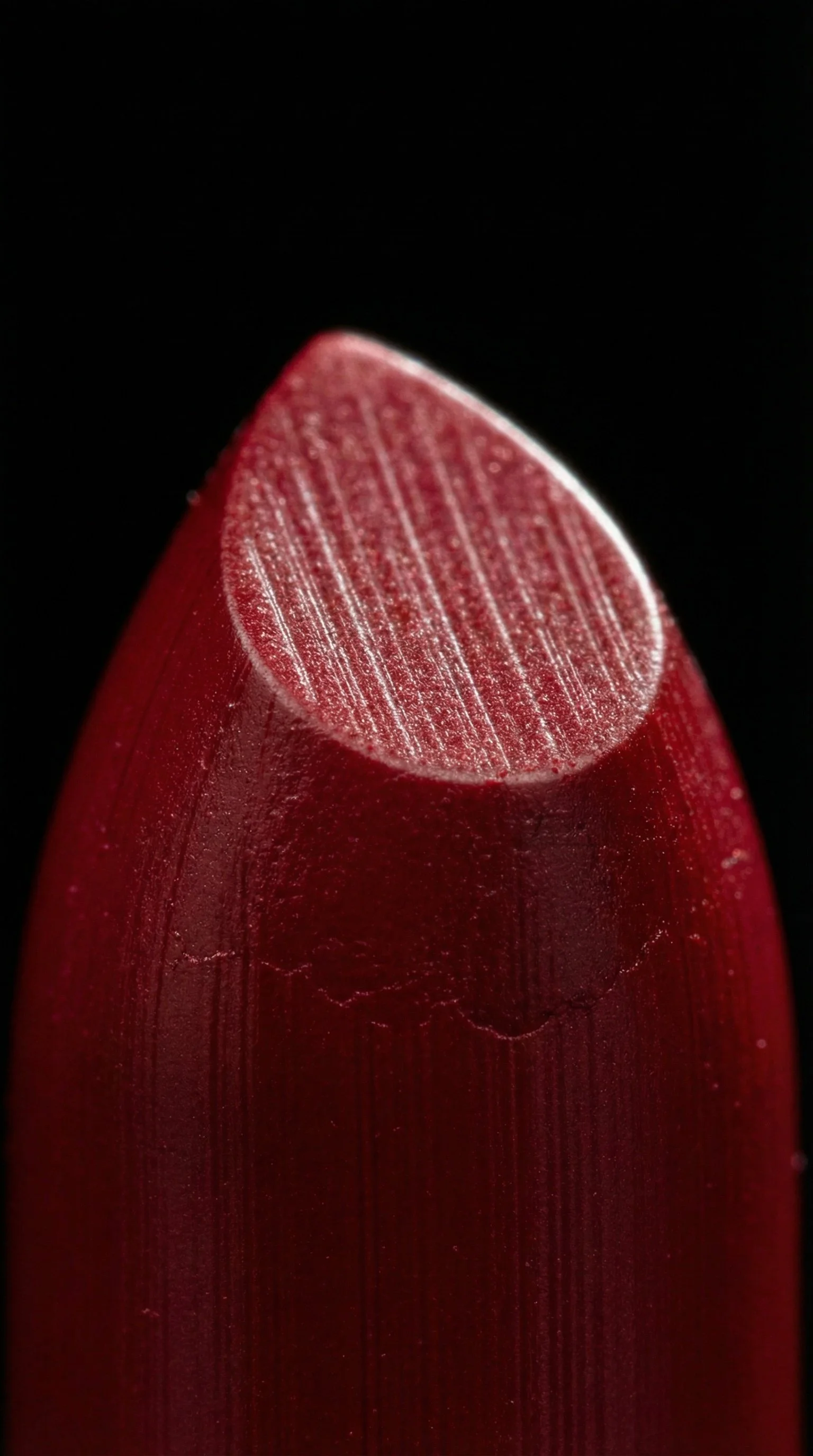 Close-up of a red lipstick tip showing texture and color contrast against a black background.