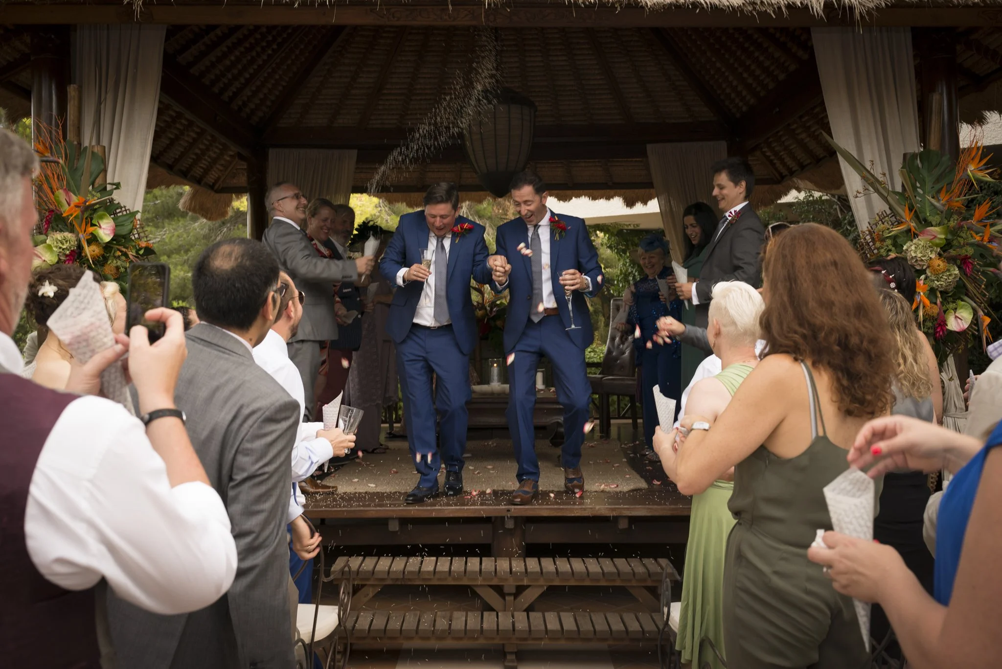 Newly married same-sex couple walking from their wedding pergola as guests applaud at a villa wedding near Moraira