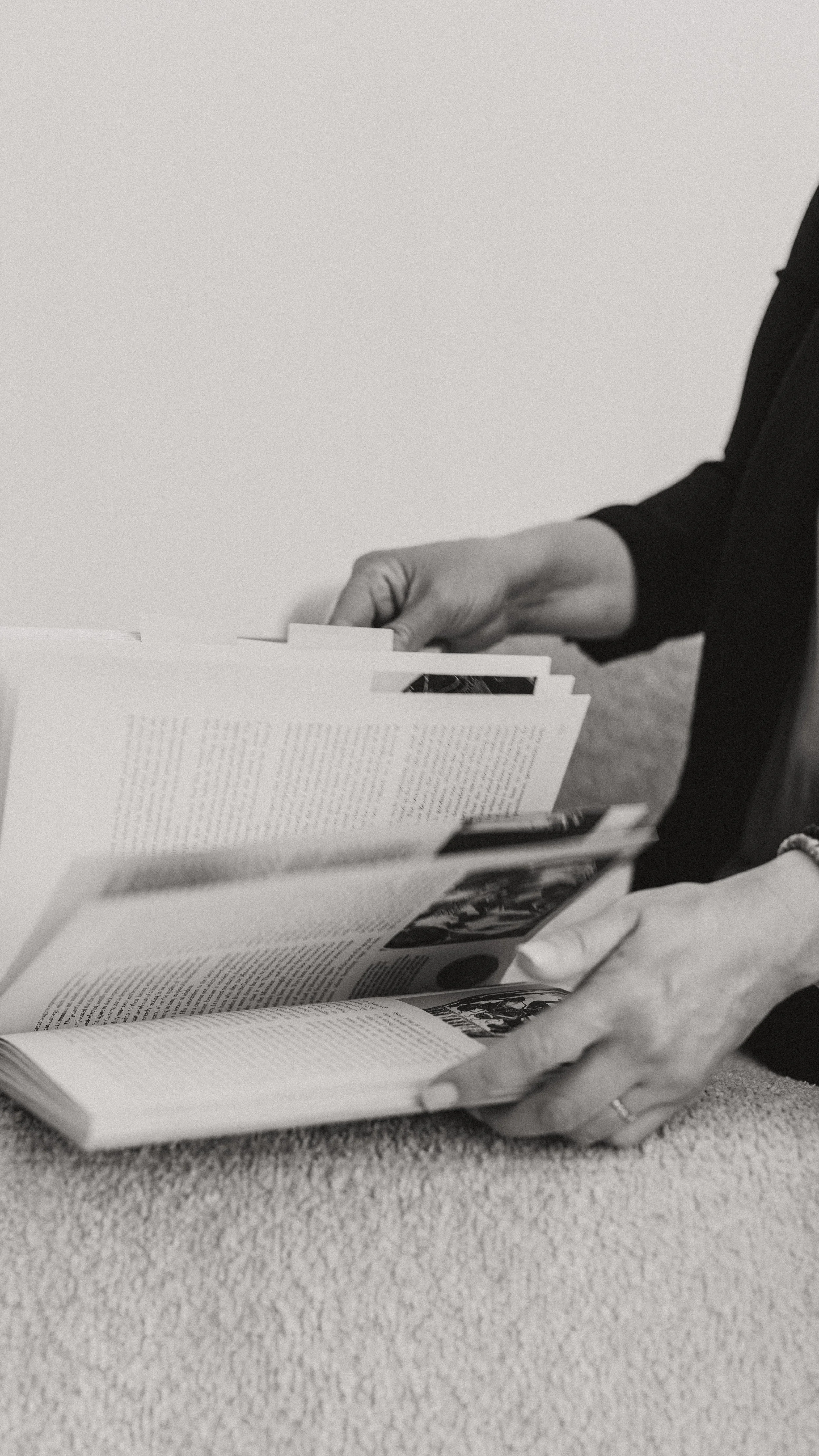 A person sitting on a carpeted floor, flipping through pages of a book or magazine.