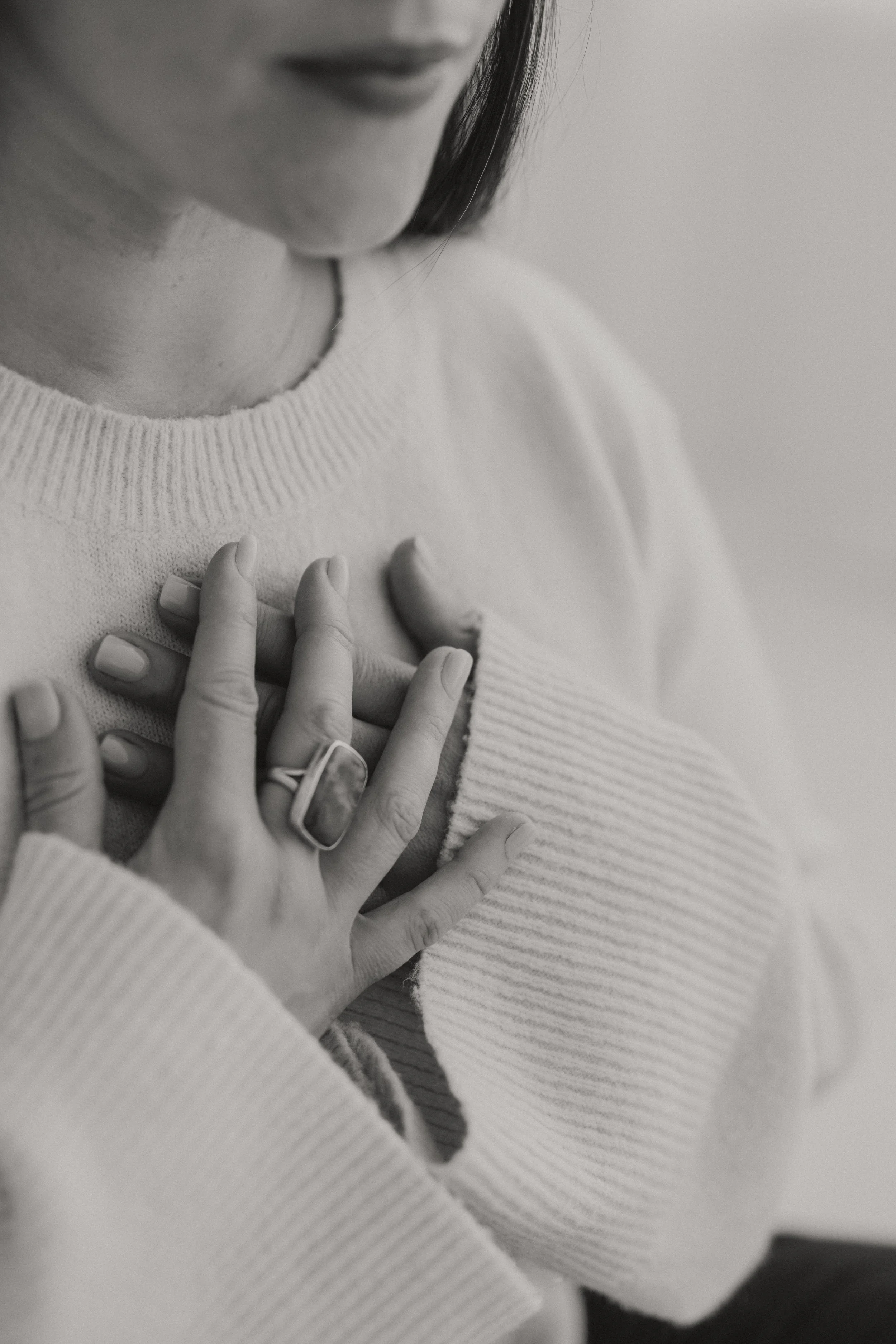 A person touching their chest with their hand, wearing a light-colored sweater, with a focus on the hand and chest area.
