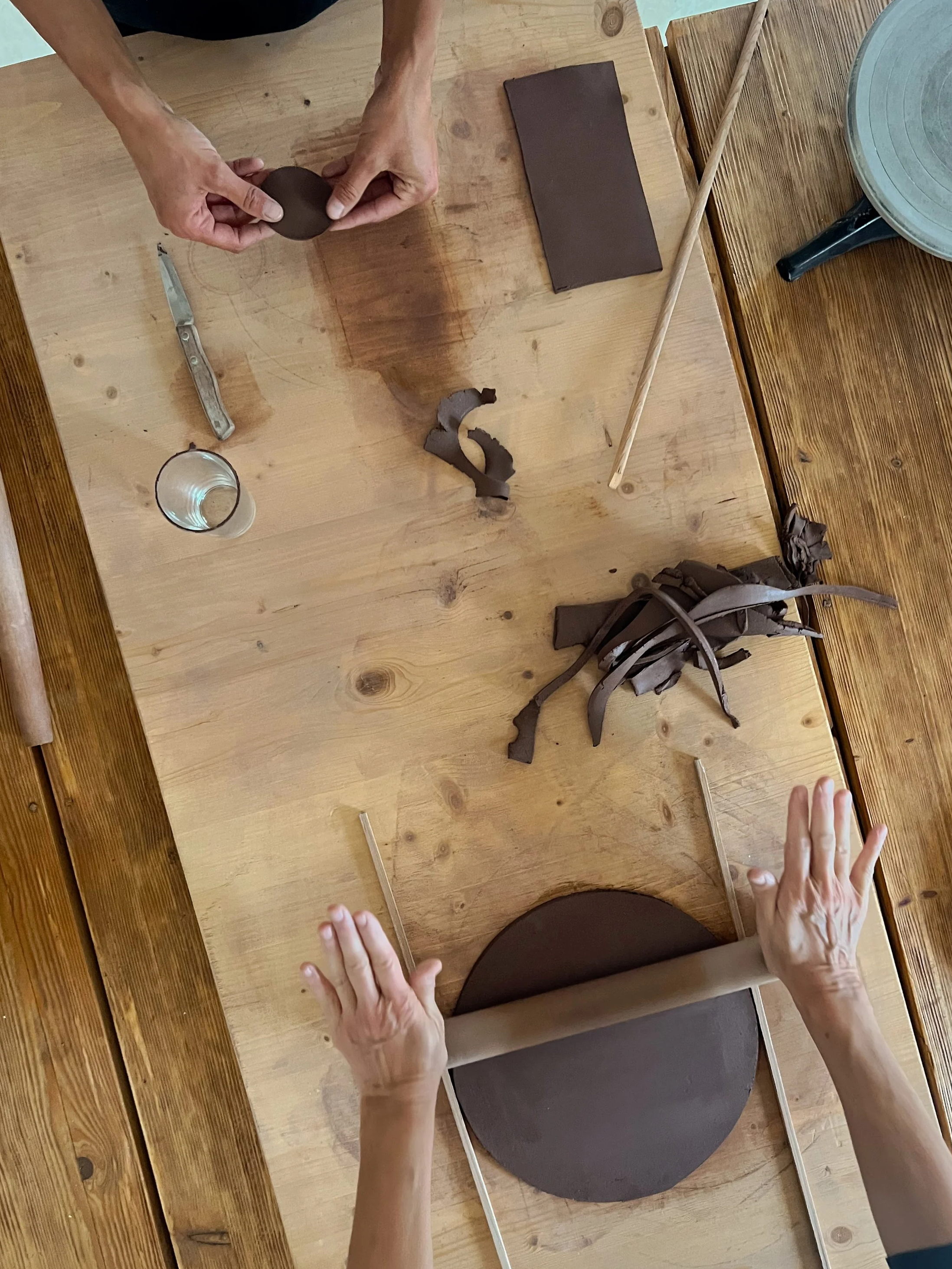 Two hands shaping a piece of ceramics on a wooden table.