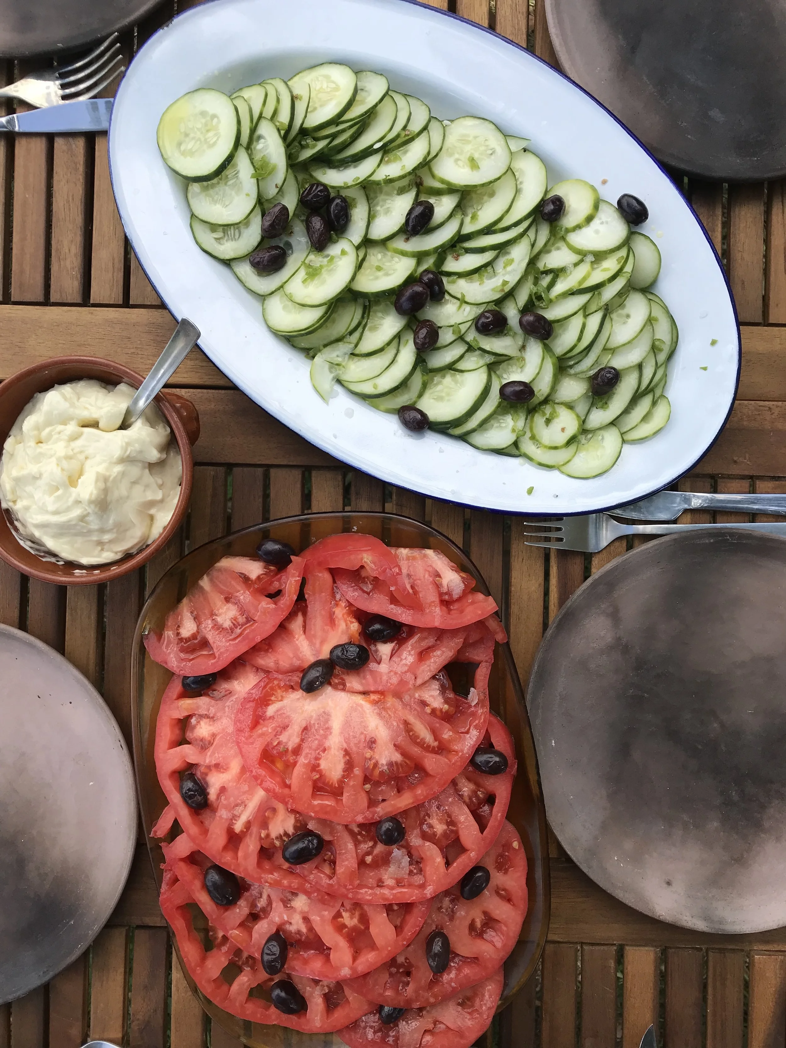 A large oval white plate with sliced cucumbers arranged in overlapping rows, garnished with black olives, placed on a wooden table.