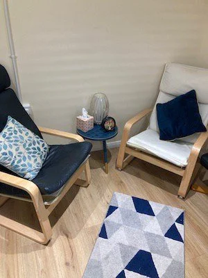 A cozy therapy room corner with two armchairs, a small side table, a decorative rug, and pillows.