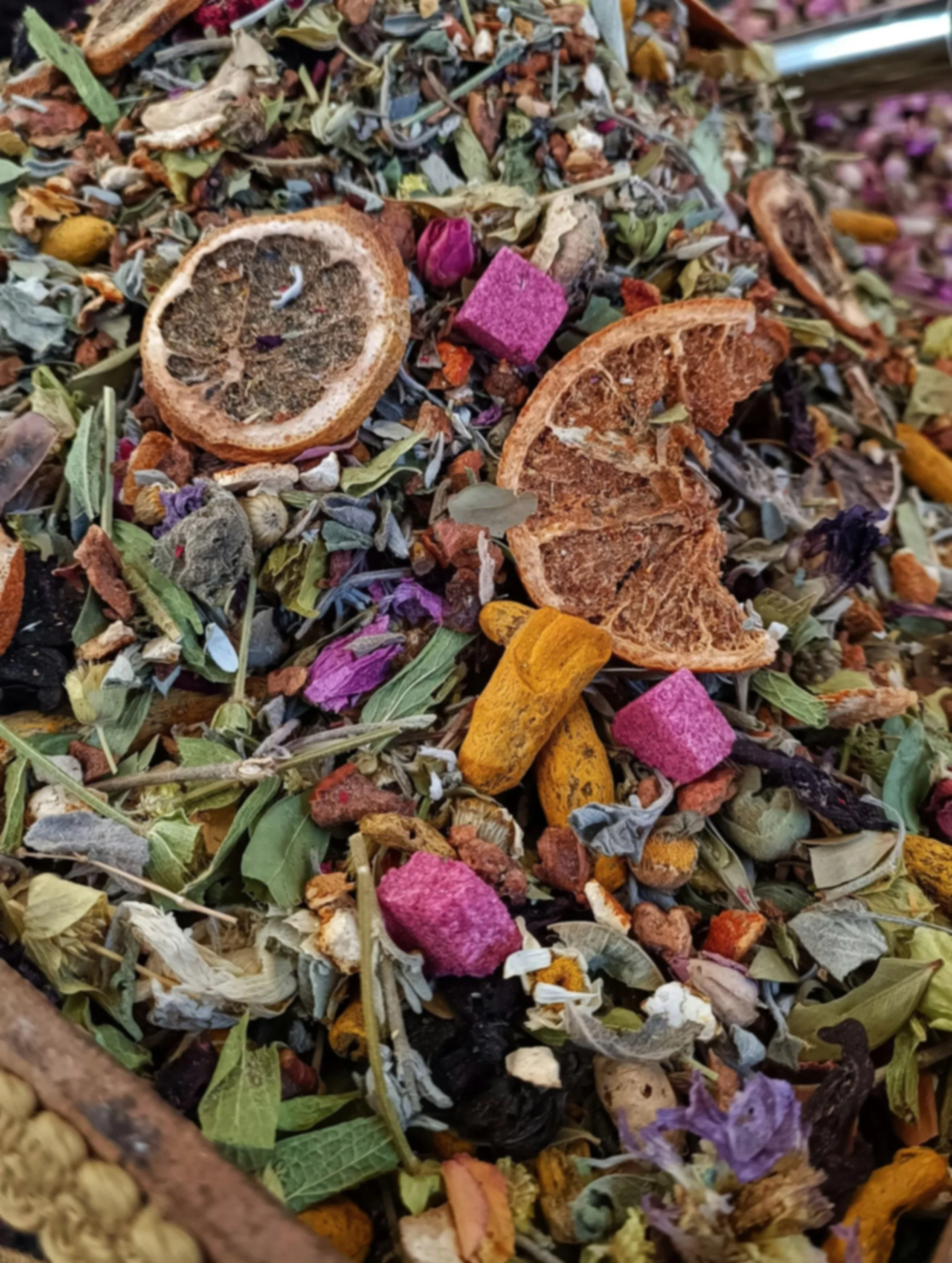 Close-up of a mixture of dried plant material, including orange splotches, purple and yellow petals, dried leaves, and pieces of dried fruit or citrus slices.