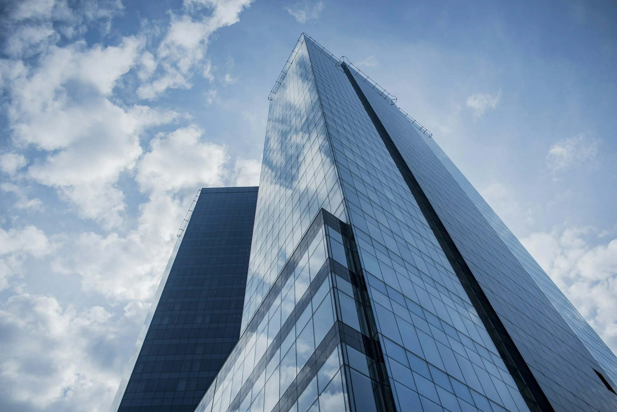 A tall modern glass skyscraper seen from below against a partly cloudy blue sky.