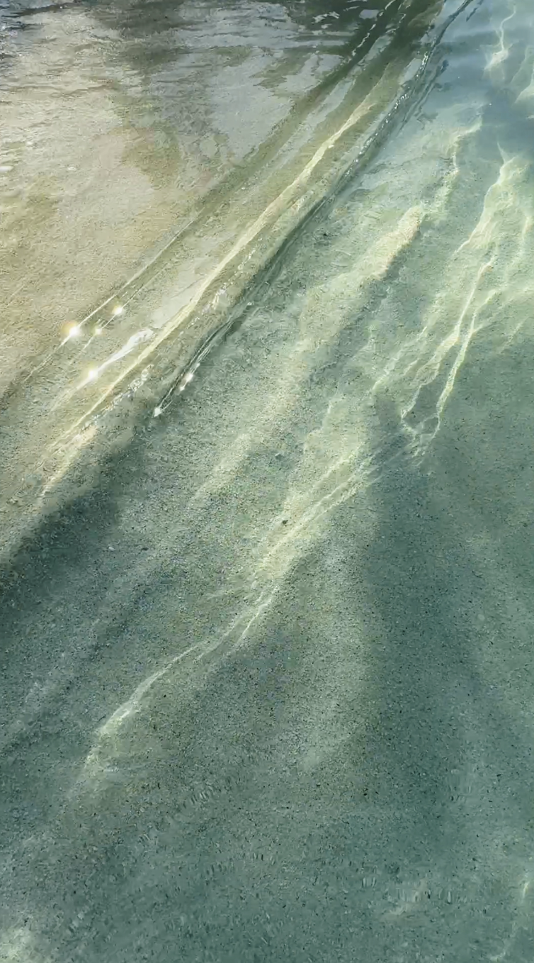 Clear water with sunlight reflections on the sandy ocean floor.