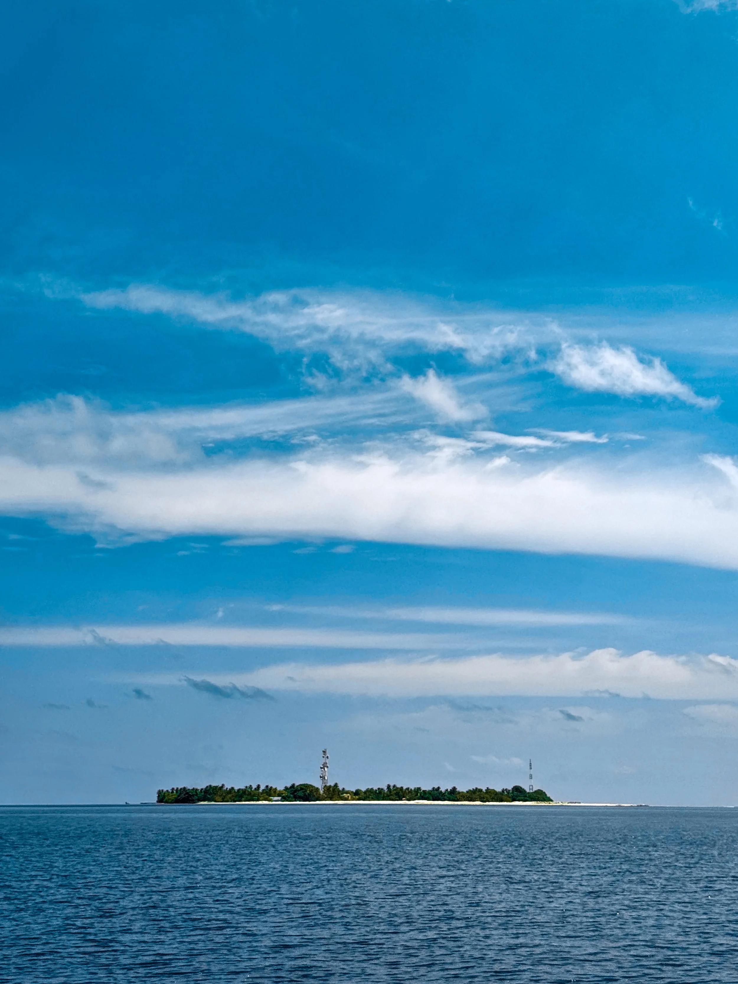 A small island with trees and communication towers is seen in the distance, surrounded by a body of water, under a partly cloudy sky.