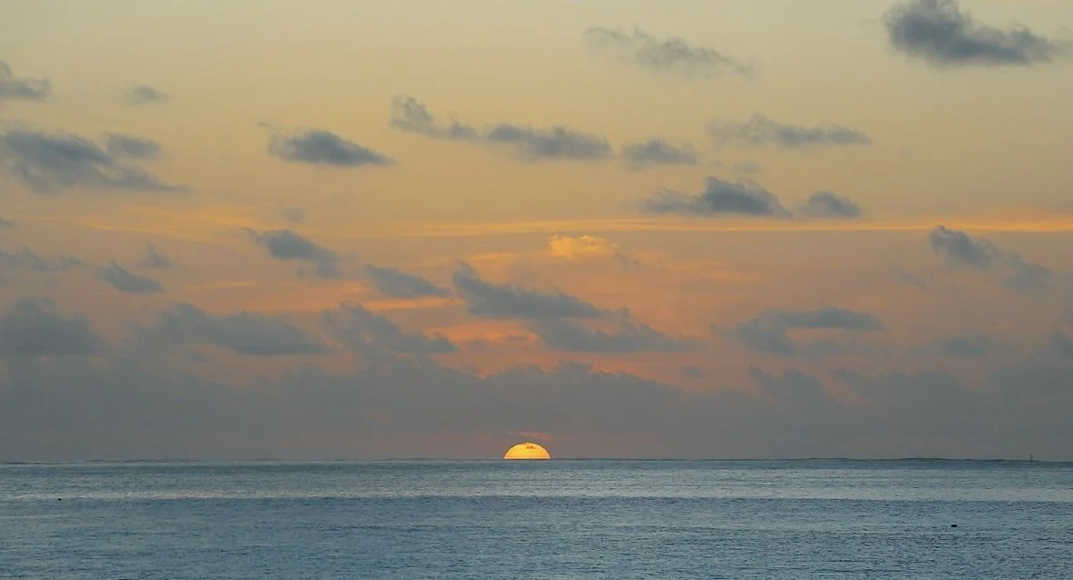 Sunset over the ocean with partially hidden sun and a partly cloudy sky.
