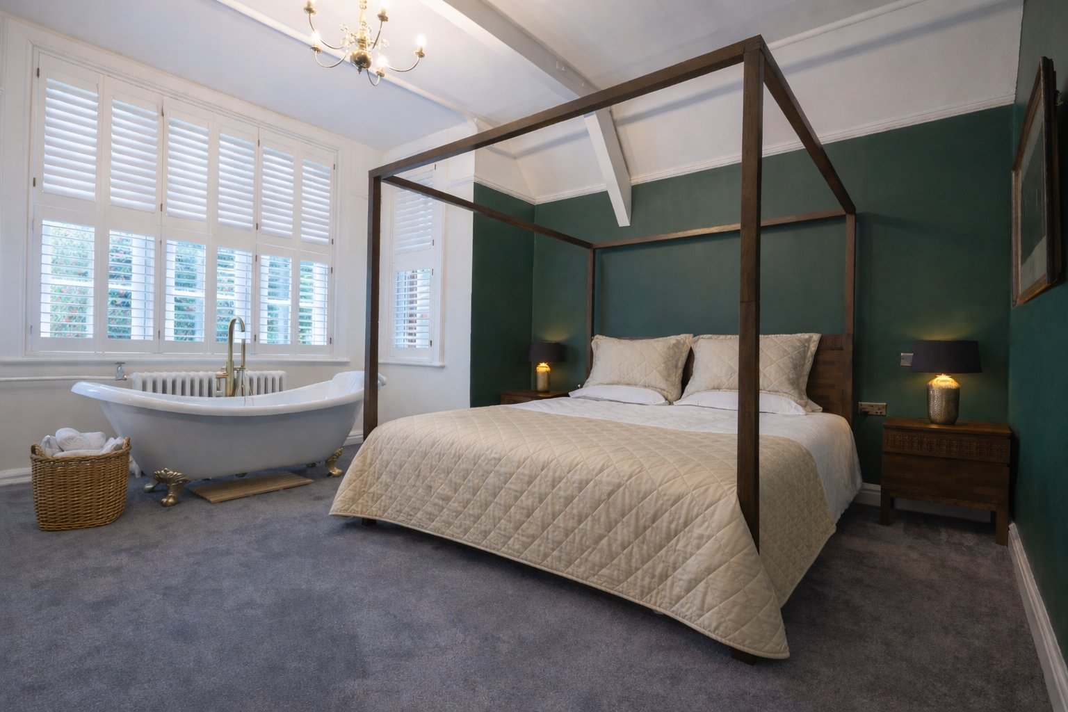 Hotel bedroom with a green accent wall, a wooden four-poster bed with beige bedding and pillows, two bedside tables with lamps, a window with white shutters, and a vintage clawfoot bathtub near the window, with a basket of towels beside it.