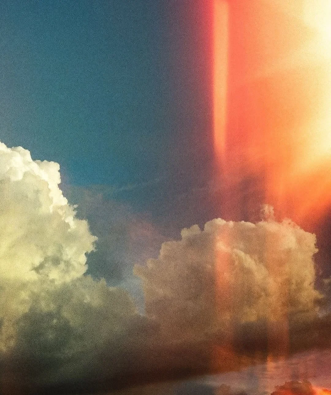 Cloudy sky with sunlight and a vertical streak of orange and red light.
