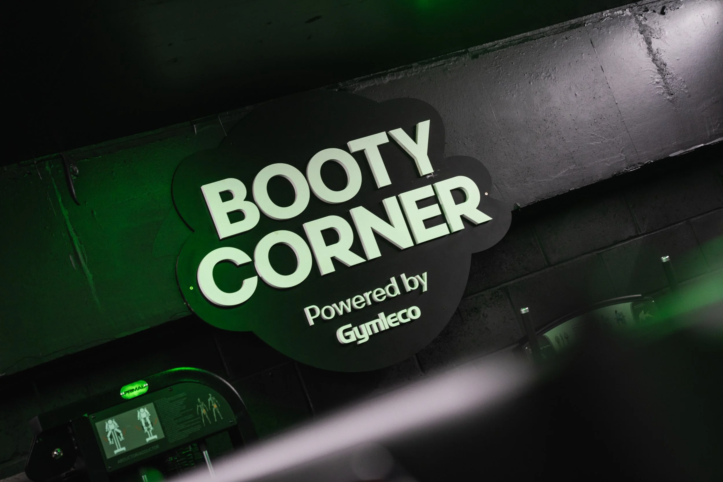 Sign reading 'Body Corners' illuminated by green lighting, with cleaning or maintenance equipment below.