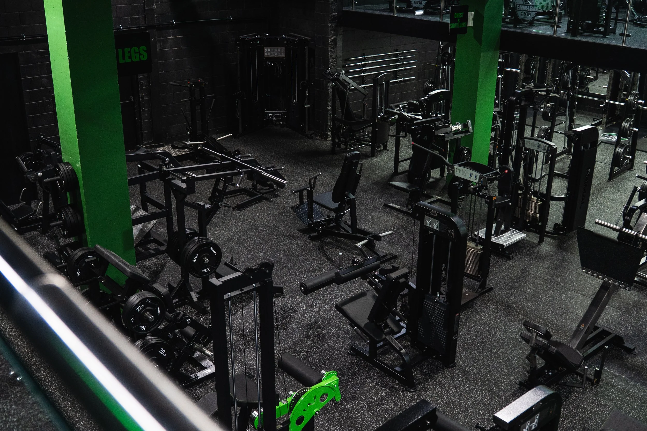 Empty weightlifting gym area with various fitness equipment, black walls, and green accents