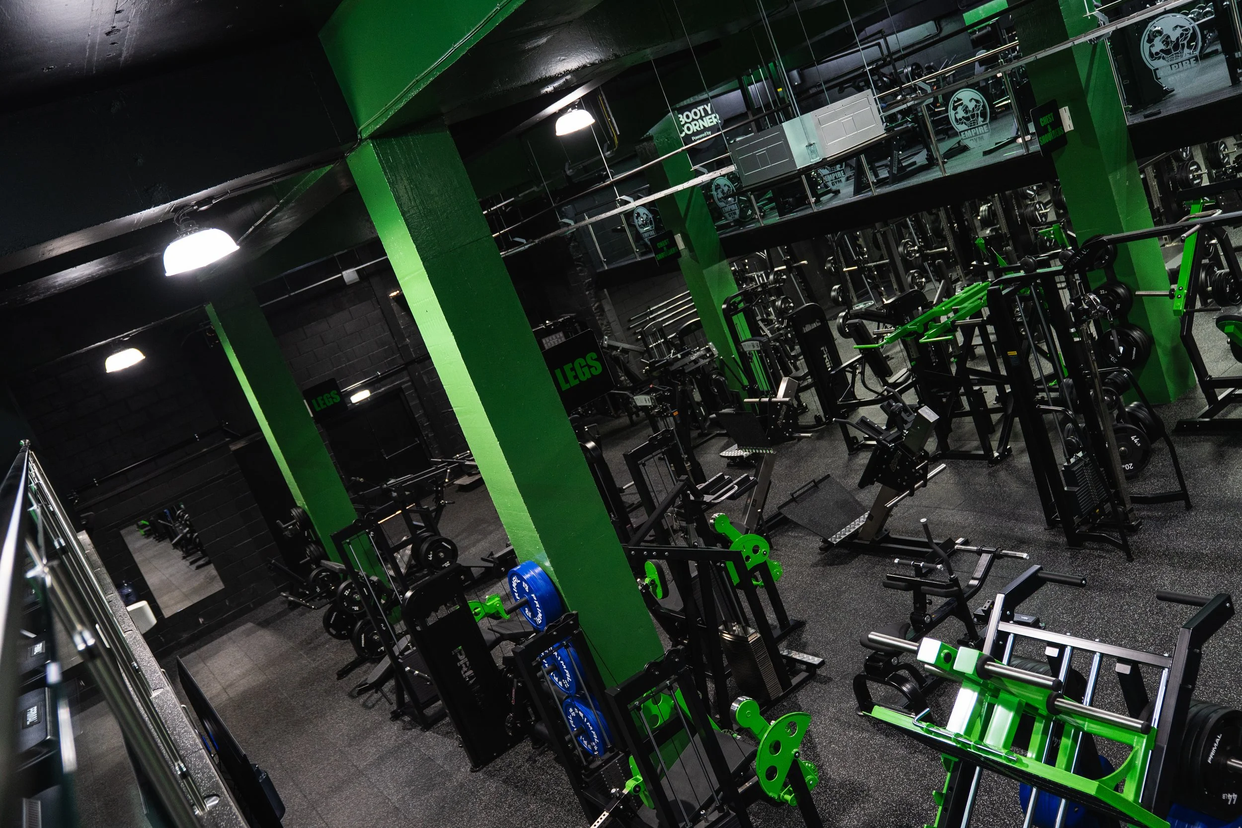 Interior of a gym with black and green equipment, mirrors, and signs labeled 'LEGS' and 'BOOTY CORNER'.