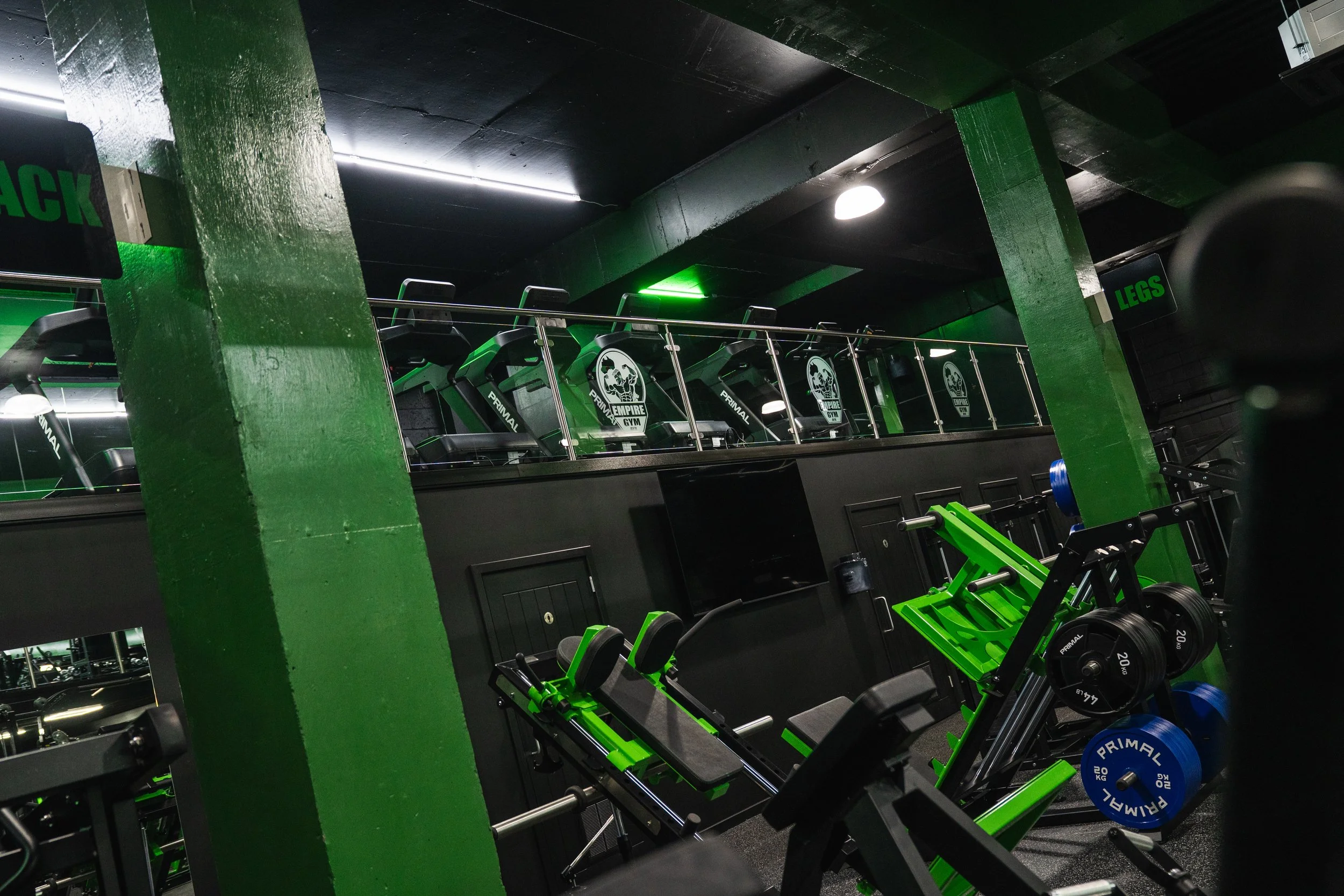 Empty gym with black and green equipment, weightlifting benches, and dumbbells, with black ceiling and green columns.