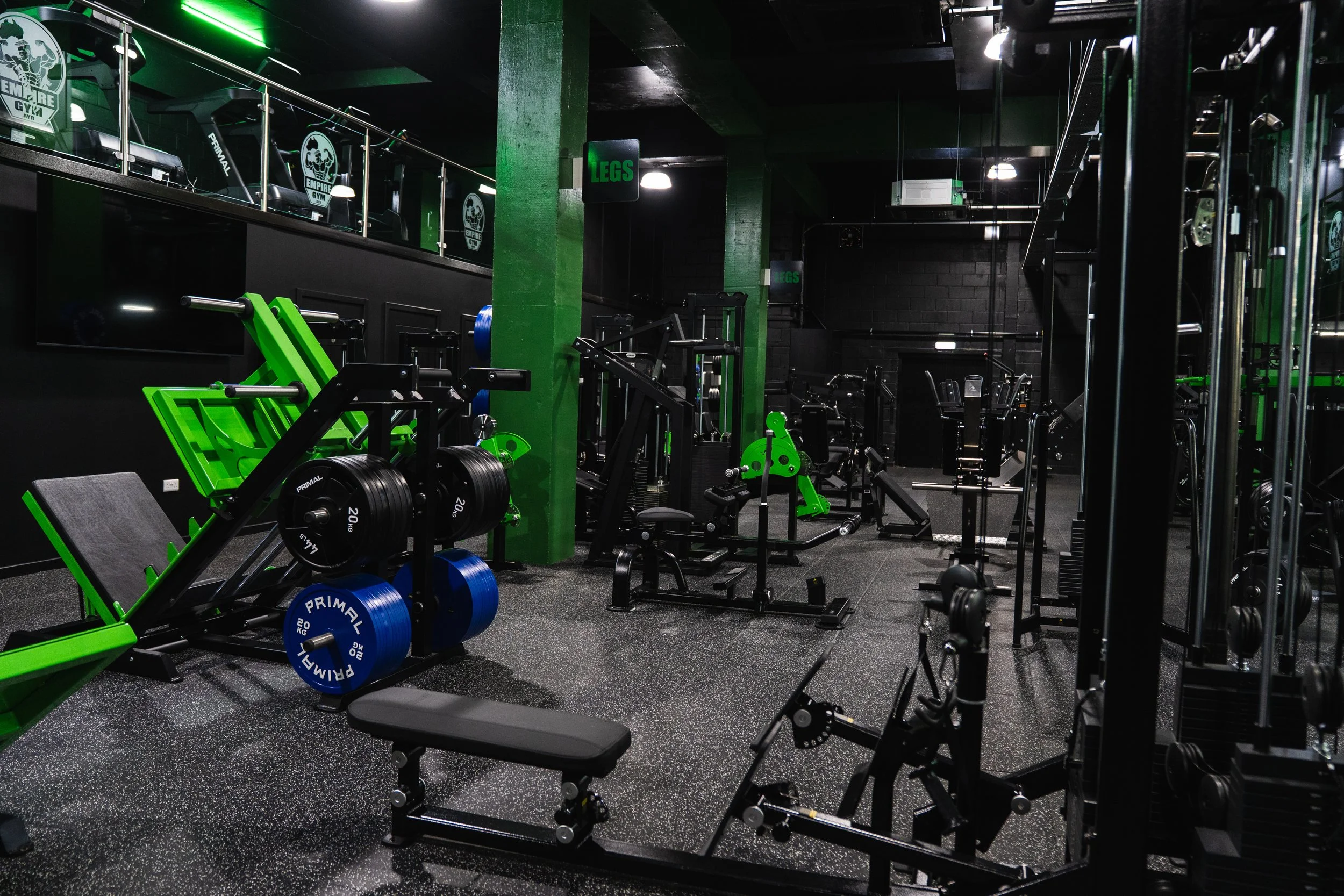 Inside a gym with black walls, green accents, and various exercise equipment, including weights, machines, and benches.