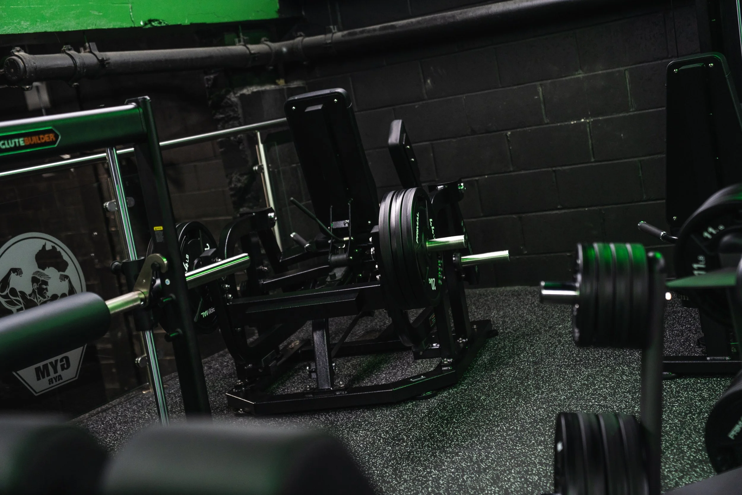 Gym gym equipment with weights, bars, and racks in a workout room with black brick walls and green accents.