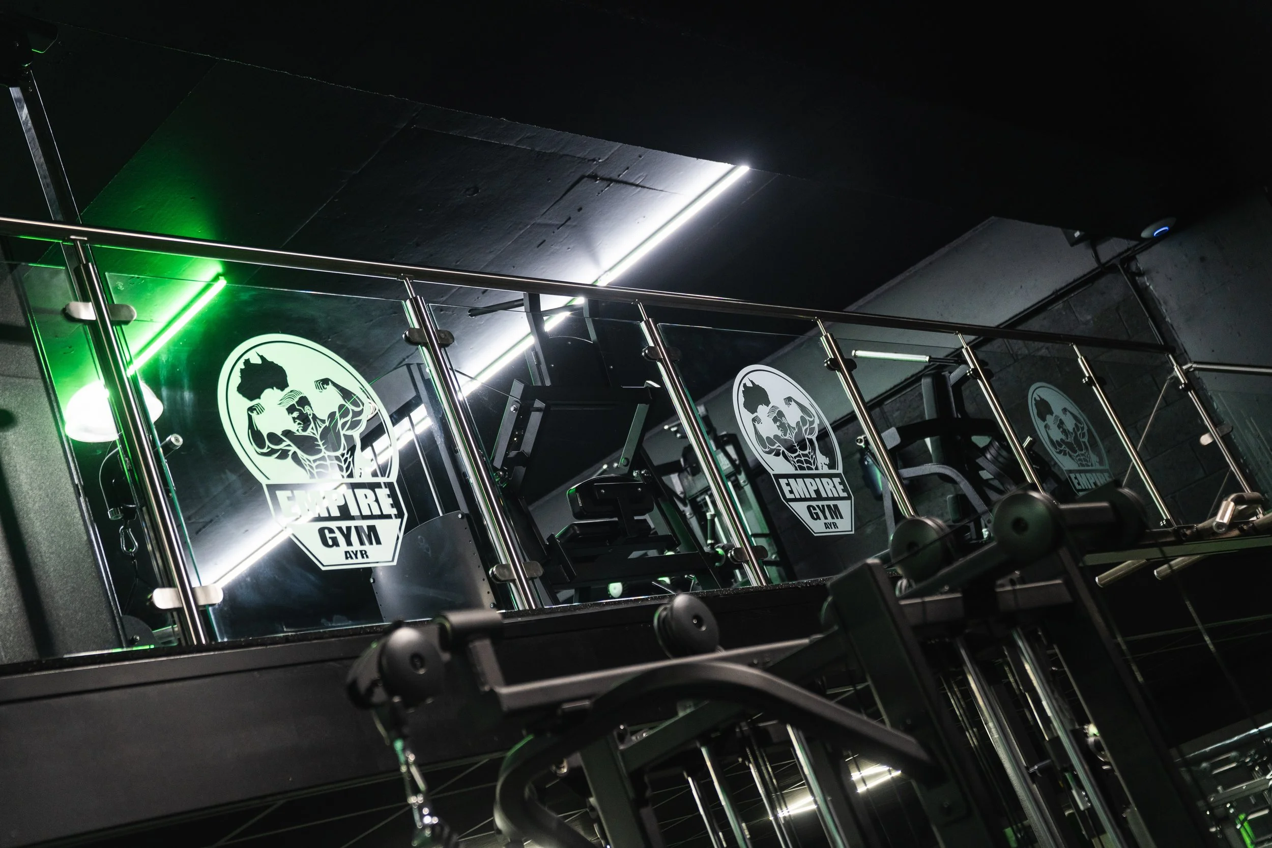Interior of Empire Gym with workout equipment, mirrors, and gym logo on glass partition.