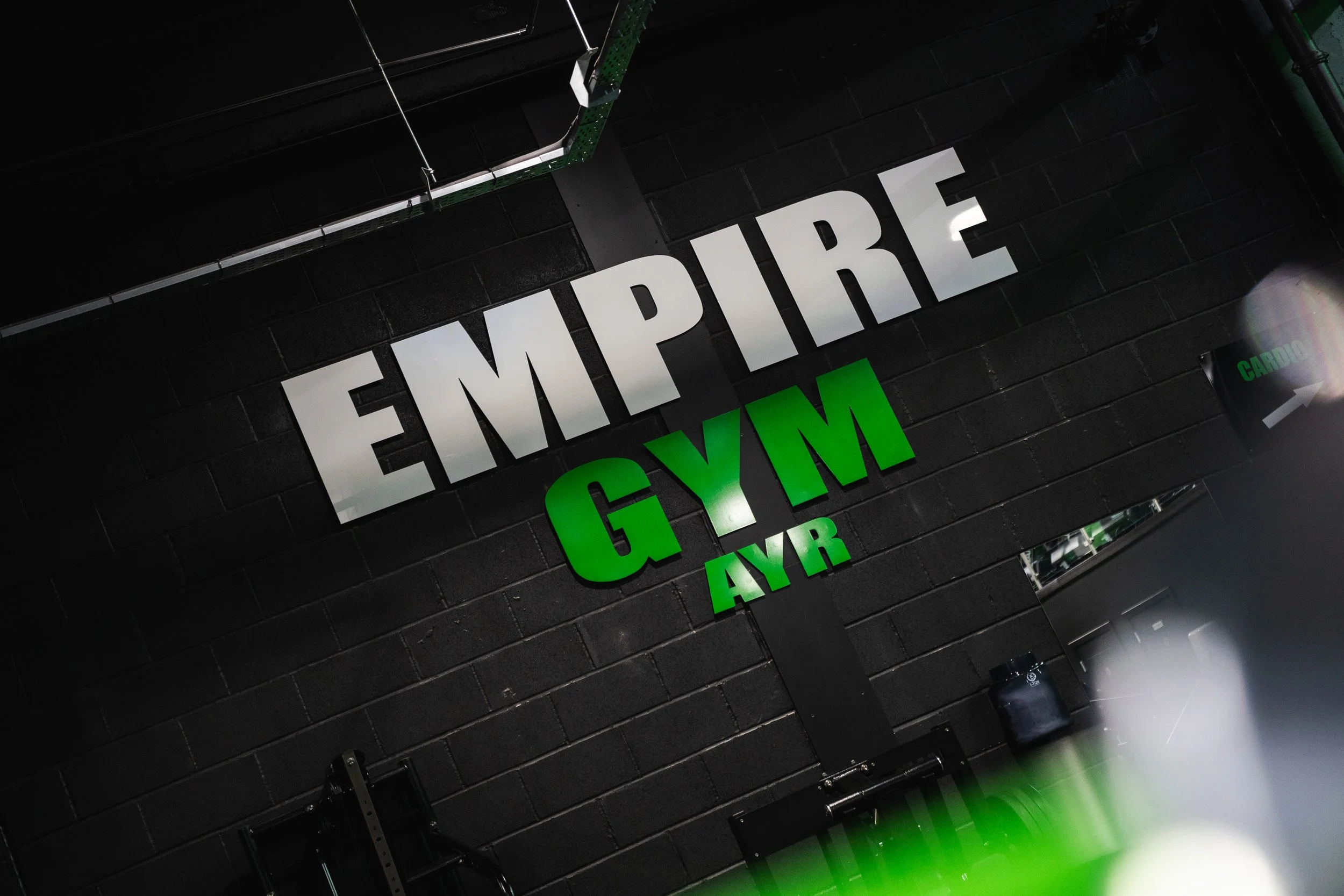 Sign that reads 'Empire Gym NYC' in black, white, and green letters on a dark wall behind gym equipment.