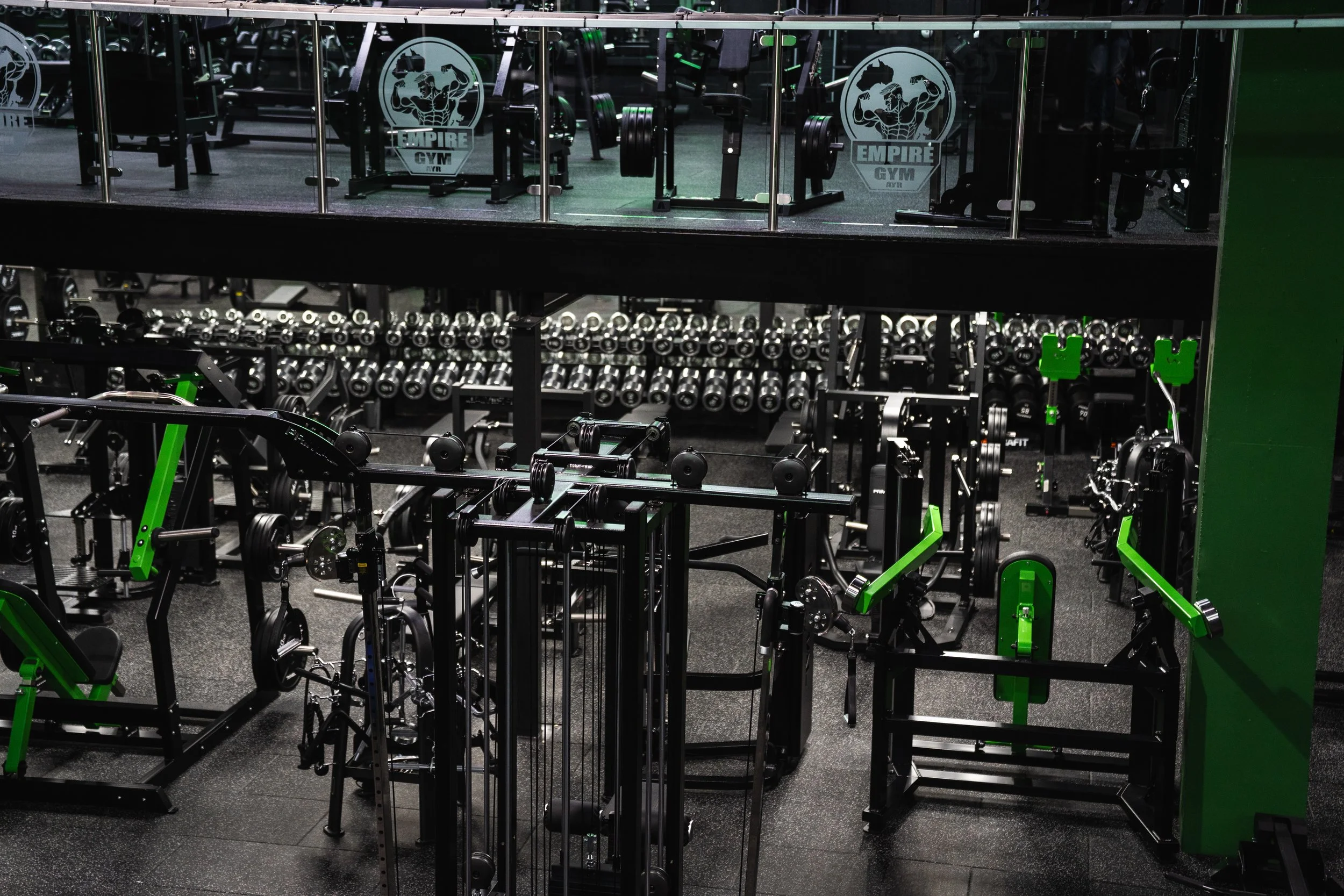 A gym with various workout equipment, including dumbbells, weightlifting machines, and cardio machines, with a logo on the mirror that reads 'Empire Gym'.
