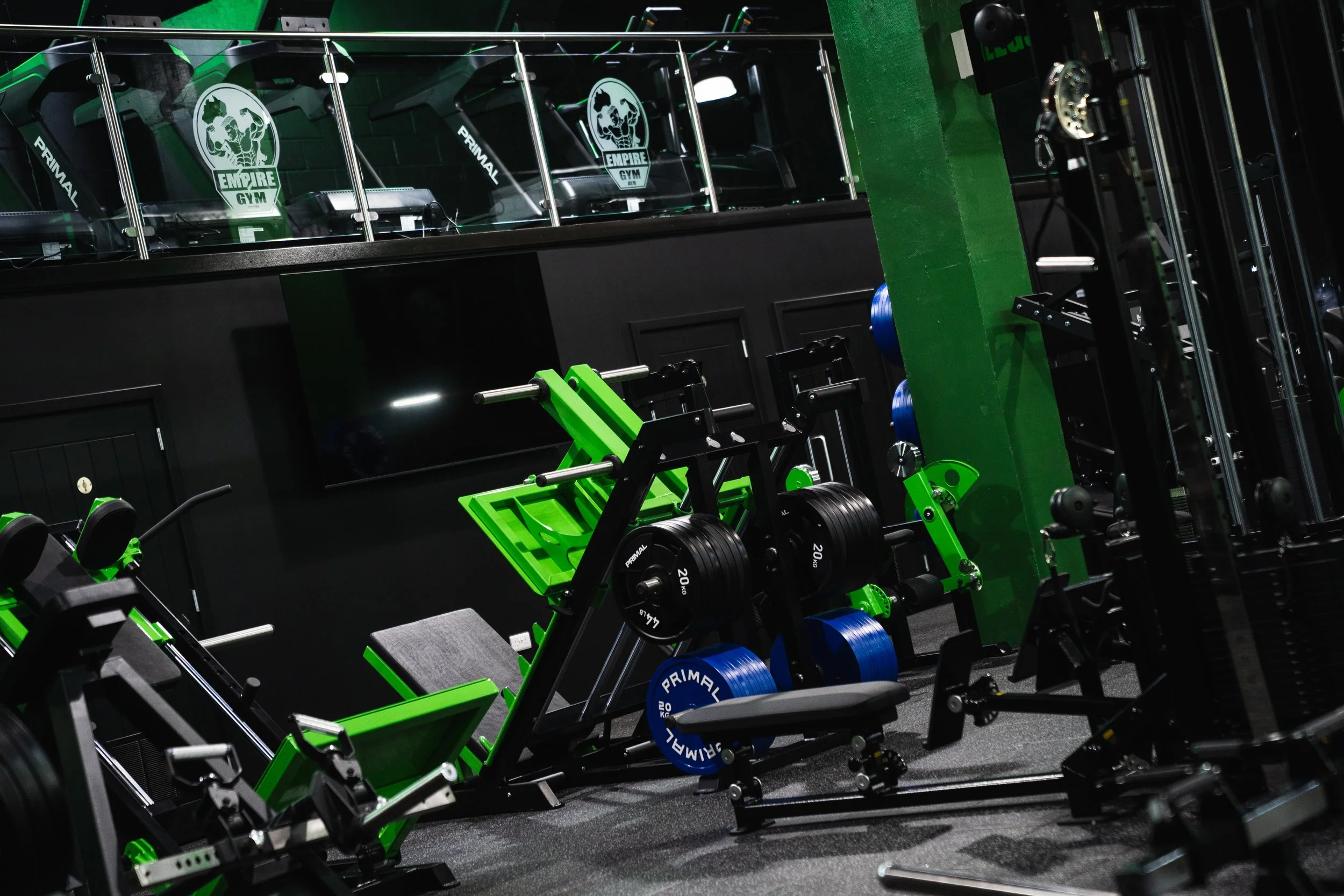 Gym equipment in a fitness studio, including weight dumbbells, adjustable benches, and a rack, with a logo that reads 'Empire Gym' on the wall.