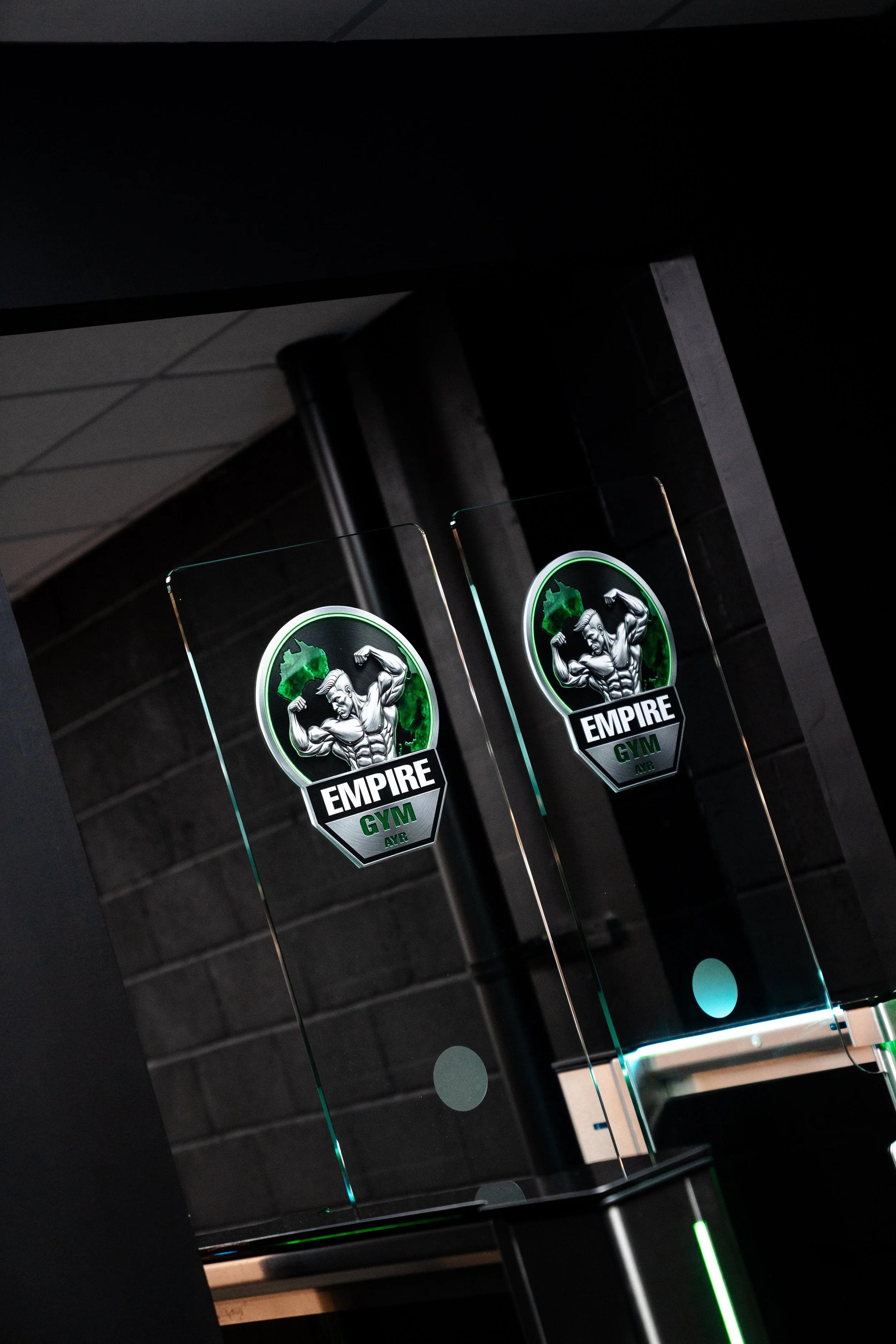 Reflection of a gym logo with a muscular man flexing his arms, surrounded by green and black colors, with the word 'EMPIRE GYM' underneath.