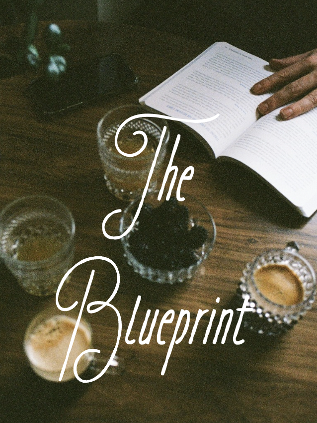 Open book, glasses, and small glasses of beverages on a wooden table during daytime.