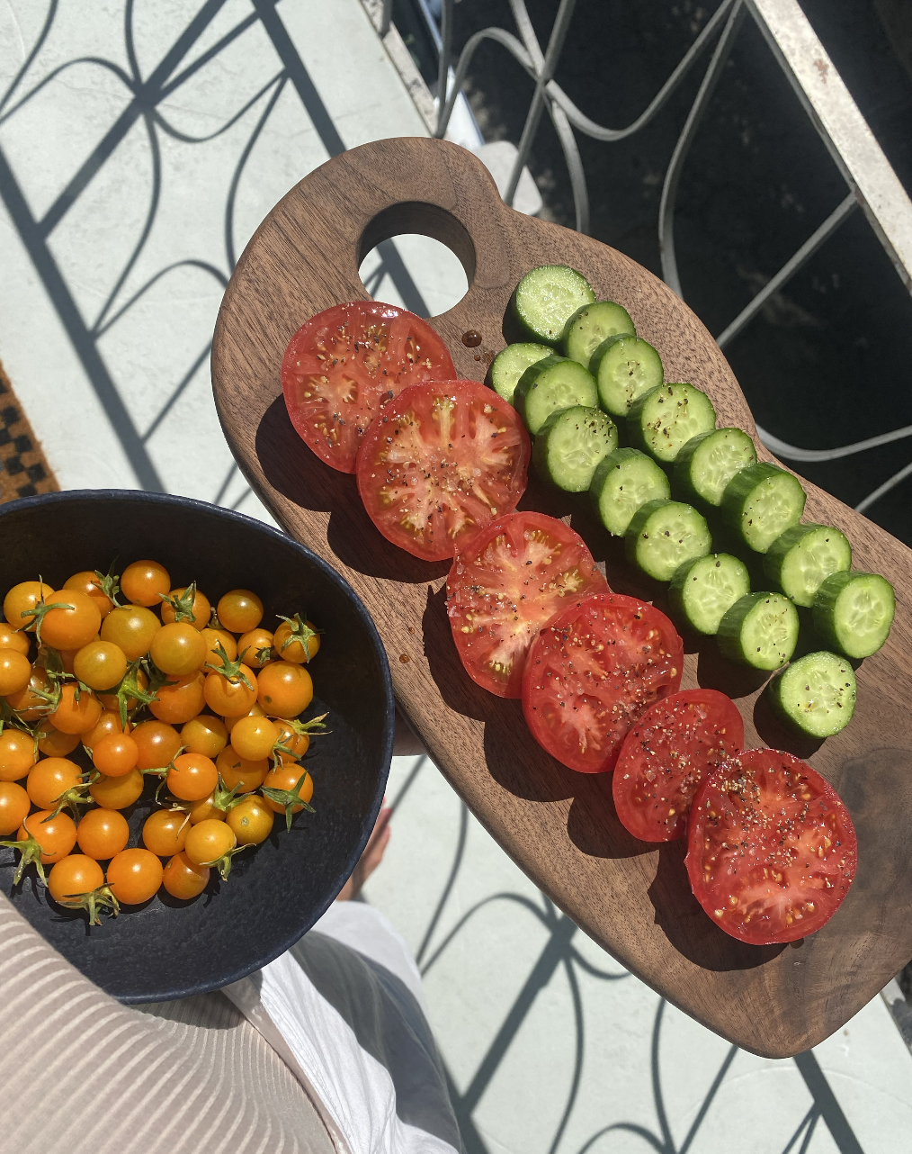 Fresh sliced tomatoes and cucumbers on a wooden cutting board, with a bowl of yellow cherry tomatoes beside it.