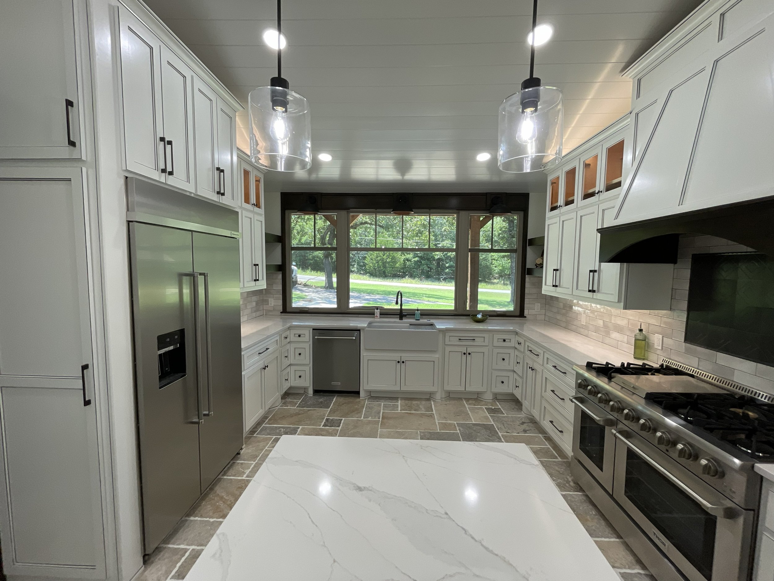 Kitchen with white cabinets, stainless steel appliances, a large window, and modern pendant lights.