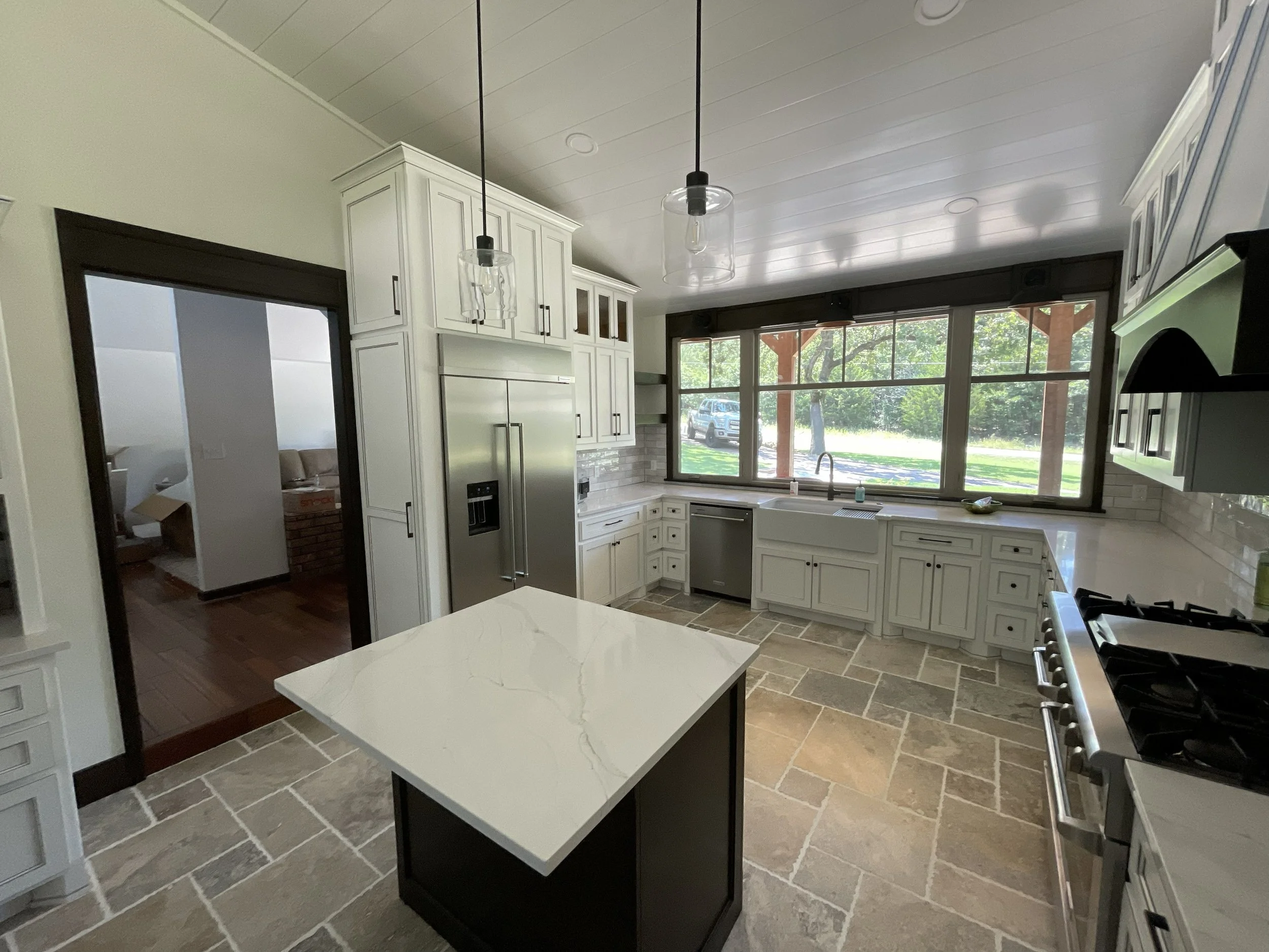 Kitchen with white cabinets, a large window overlooking a yard, gray tiled floor, and two modern pendant lights hanging from the ceiling.