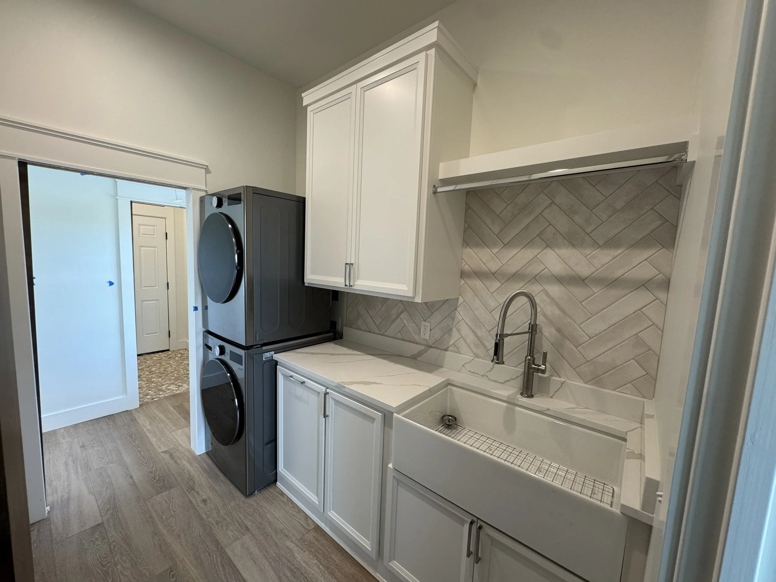 Laundry room with white cabinets, gray washer and dryer, and beige herringbone tile backsplash.