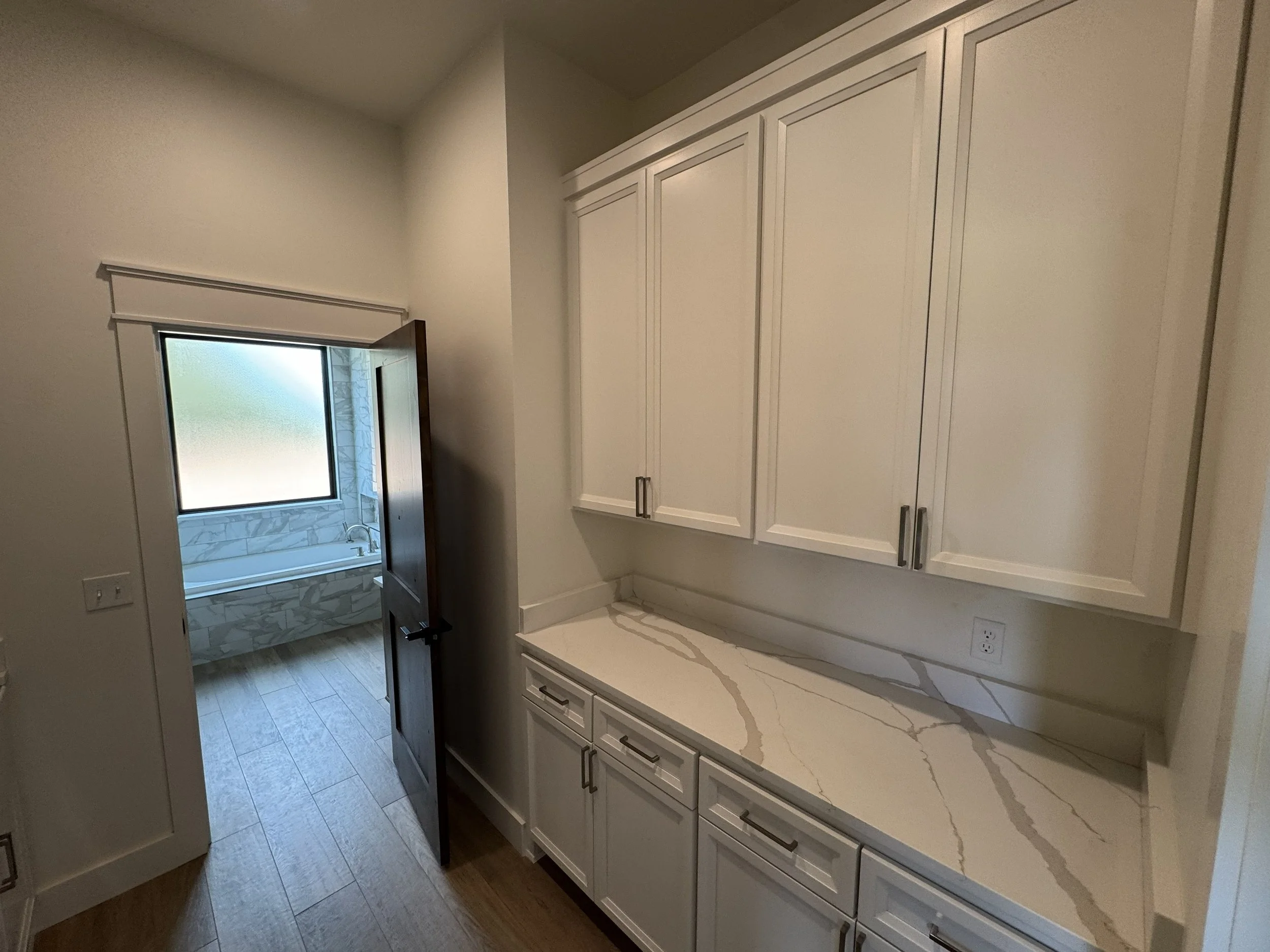 Kitchen with white cabinets and marble countertop, small window above the sink, and a door leading outside.