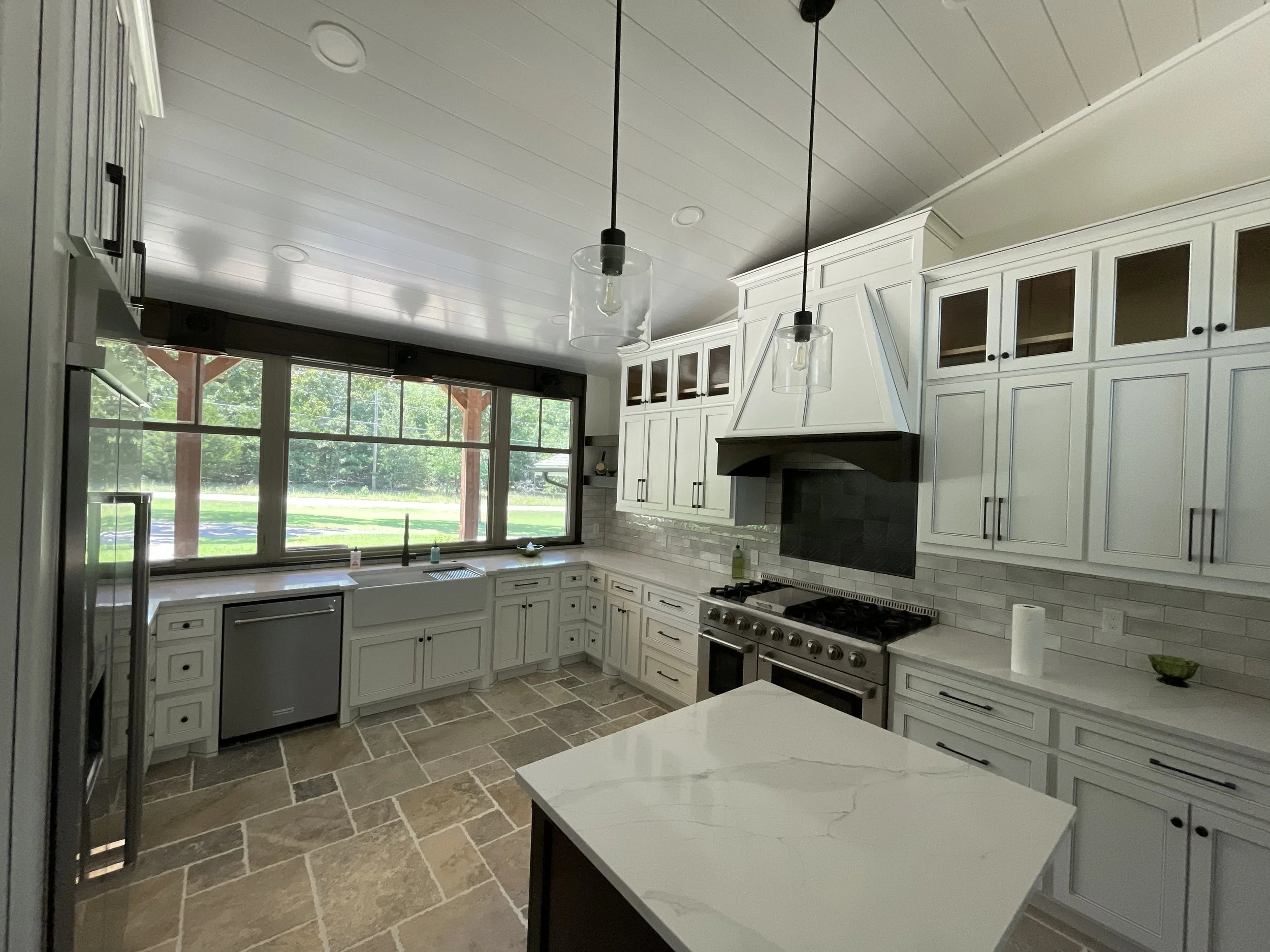 Modern kitchen with white cabinets, black hardware, a large window, and pendant lights hanging from a white ceiling.