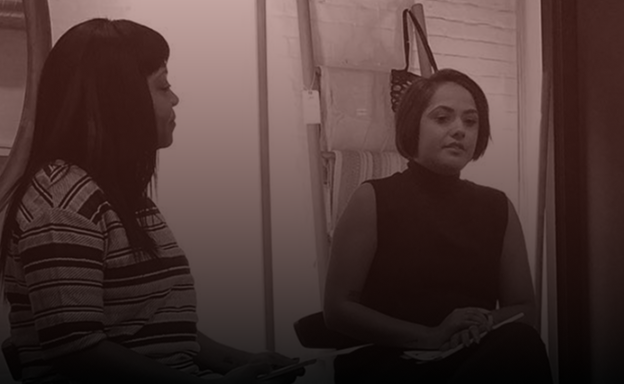 Two women sitting indoors, engaged in conversation.