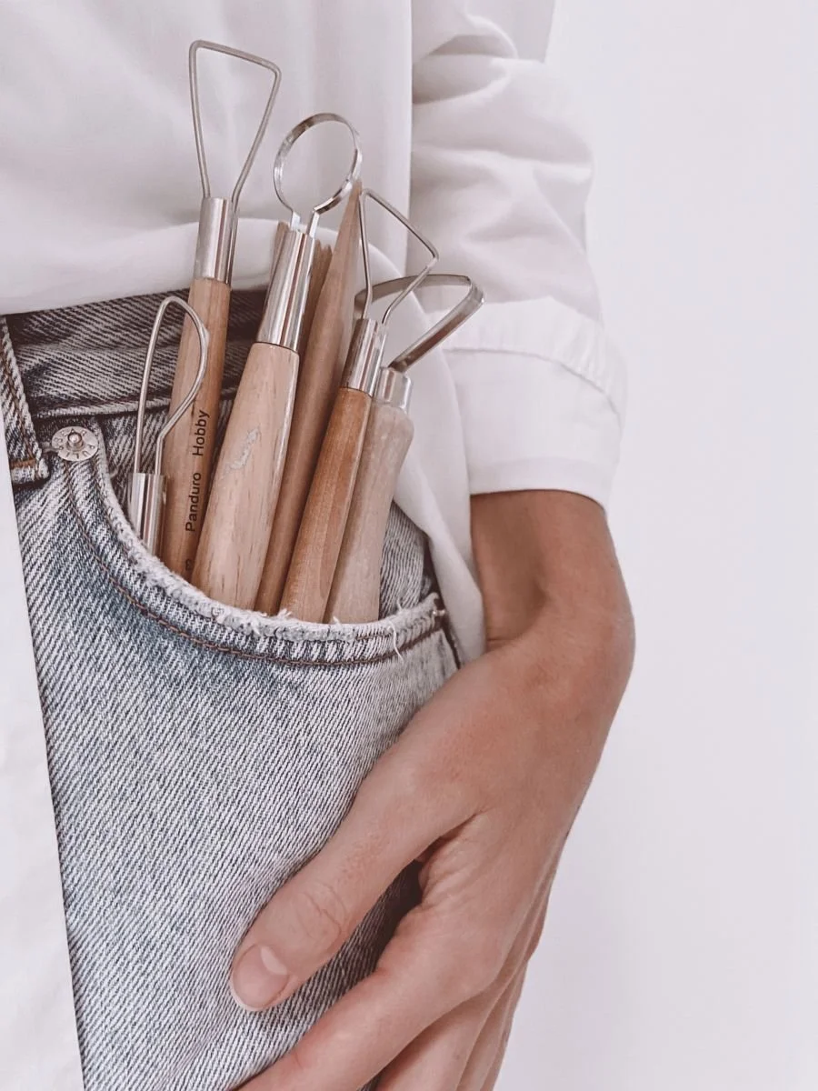 A person wearing jeans and a white shirt holding a pocket full of clay sculpting tools.