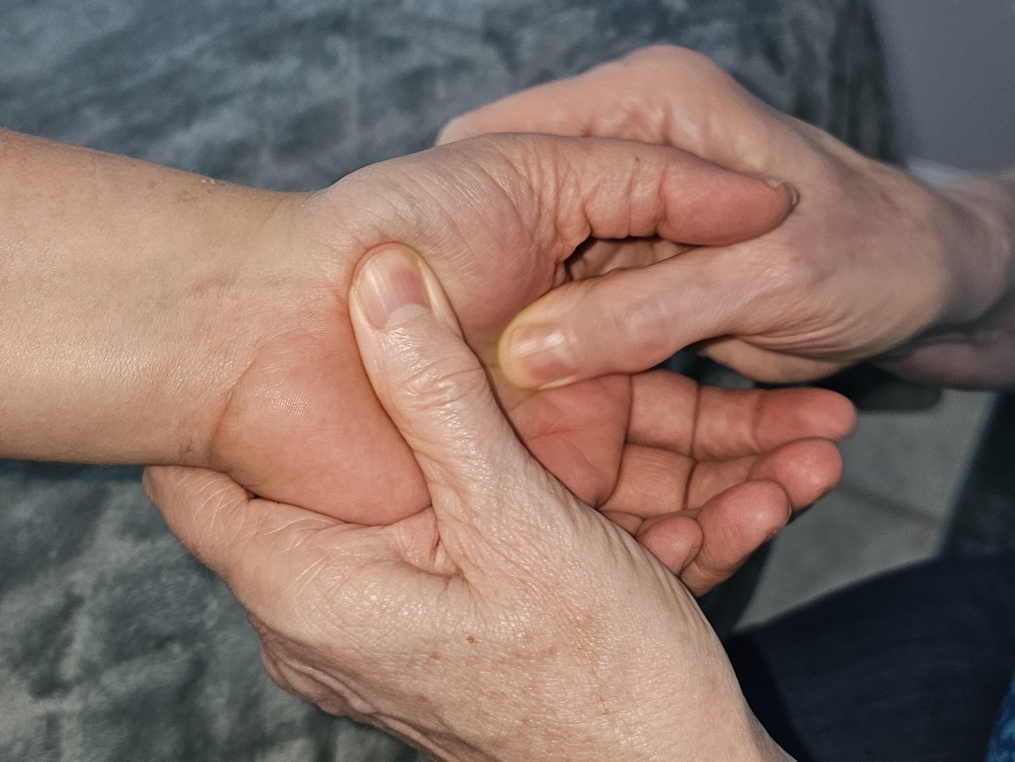 Two hands holding each other, one appears older with more wrinkles and visible veins, and the other younger with smoother skin.