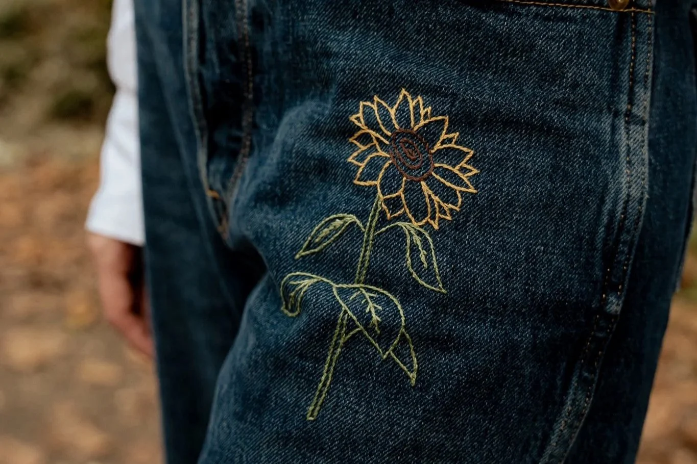 Close-up of denim jeans with sunflower embroidery on the thigh.