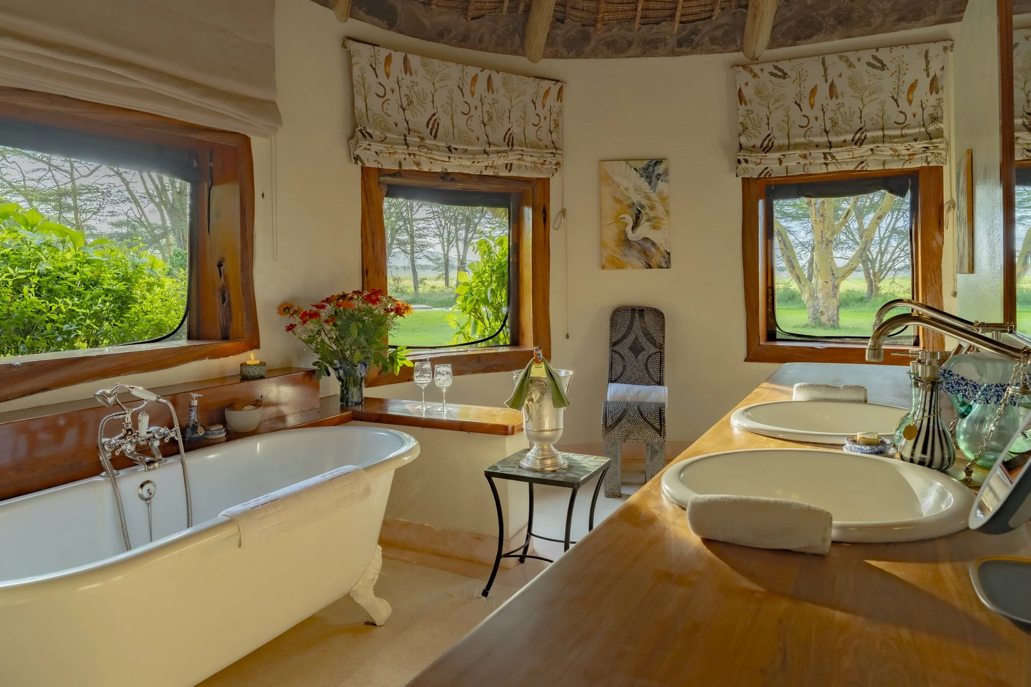 Beautiful and airy bathroom with a bathtub set up for a leisurely bath with champagne, candles and flowers and views of the trees and greenery.