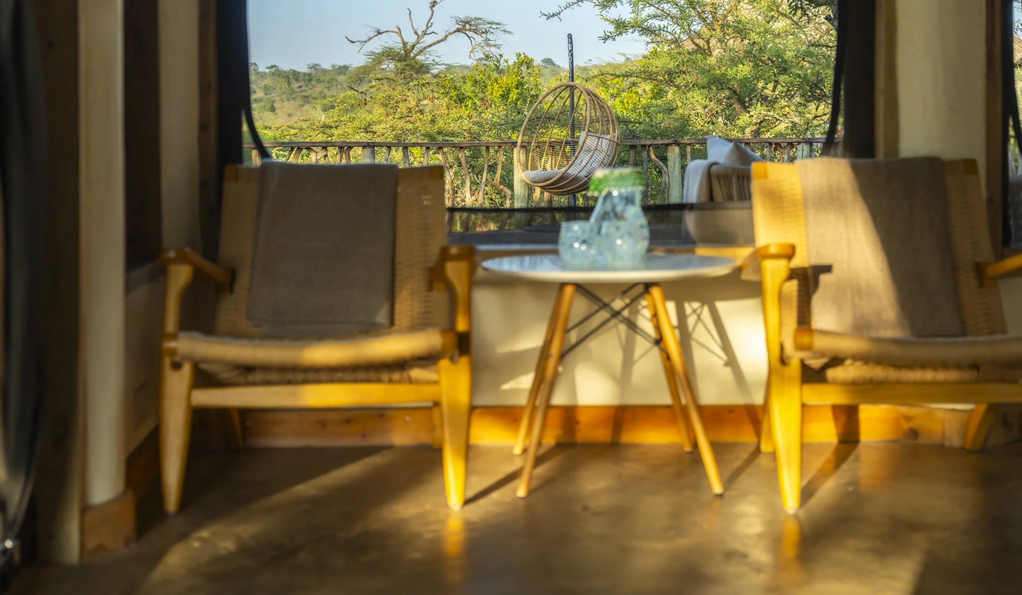 View of an outdoor balcony with a hanging wicker chair and trees in the background.