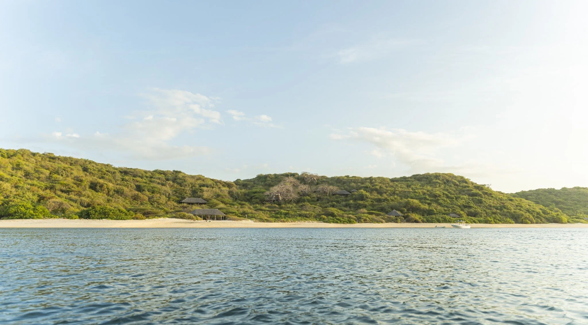 A scenic view of a body of water with a lush, green hillside in the background and several small huts nestled among the trees.