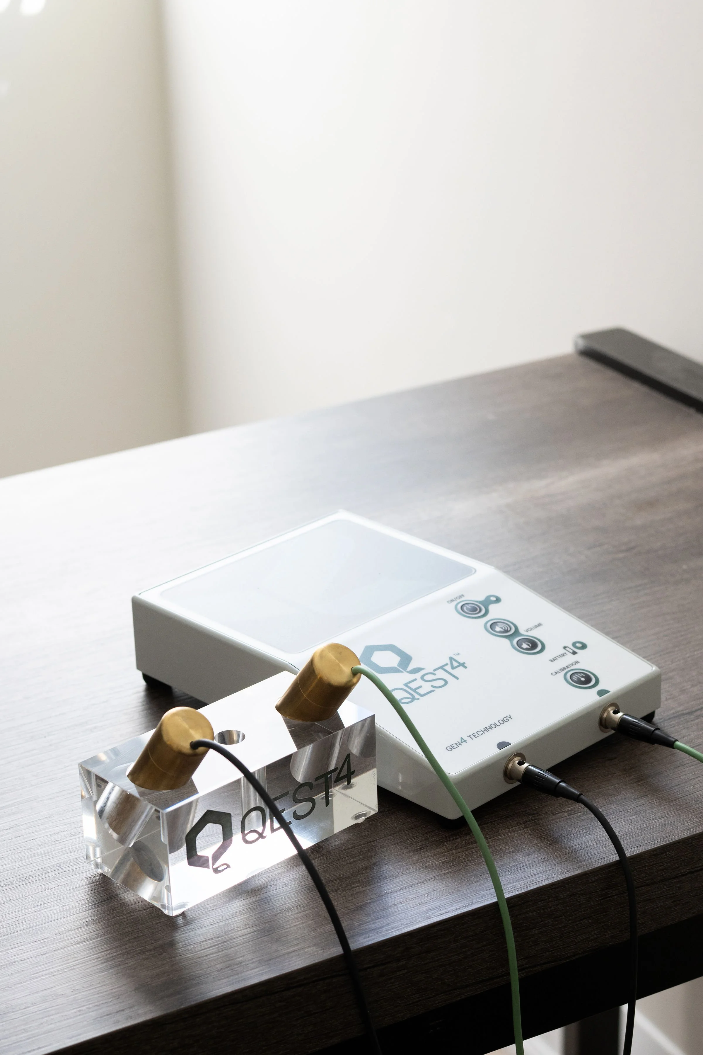 Scientific equipment on a wooden table, including a clear acrylic block with black text, and a device labeled "QRS T4" with probes connected by cables.