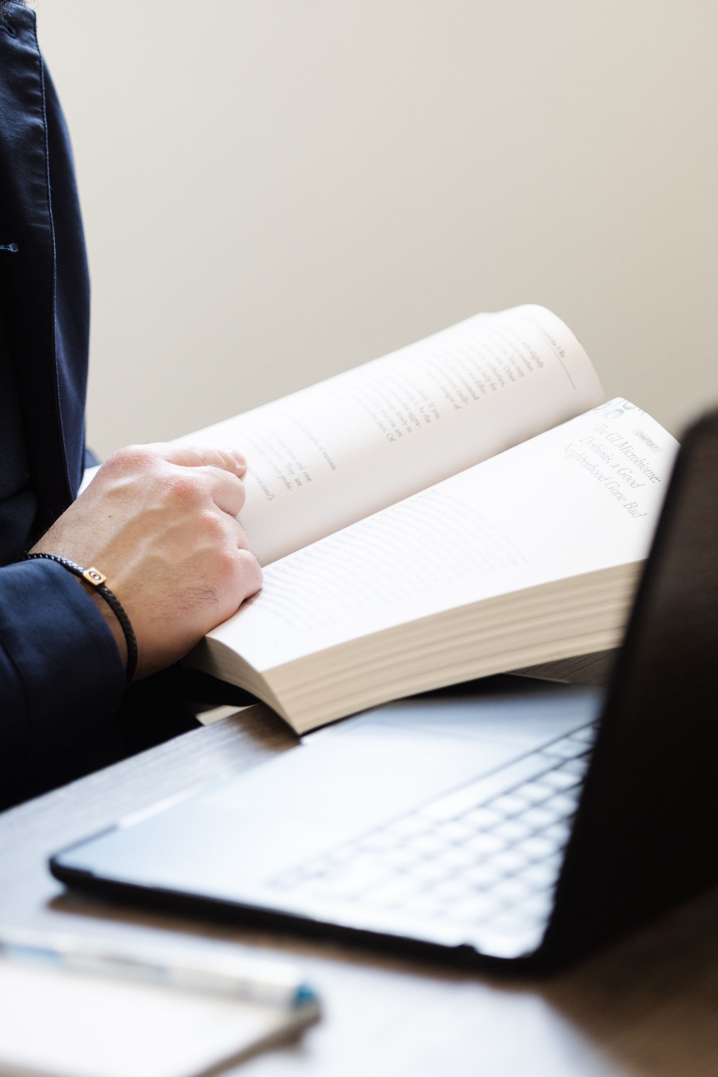 Person holding a book with a white cover and reading glasses resting on a desk.