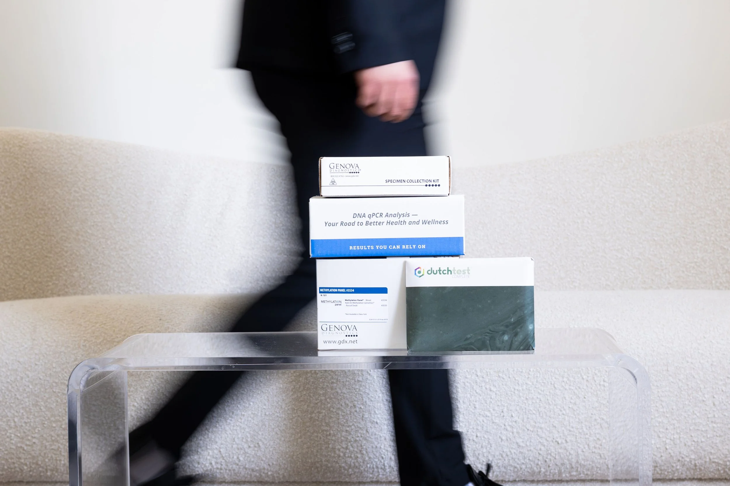 Four stacks of medical testing kits on a table, with a person's arm and hand visible in the background.