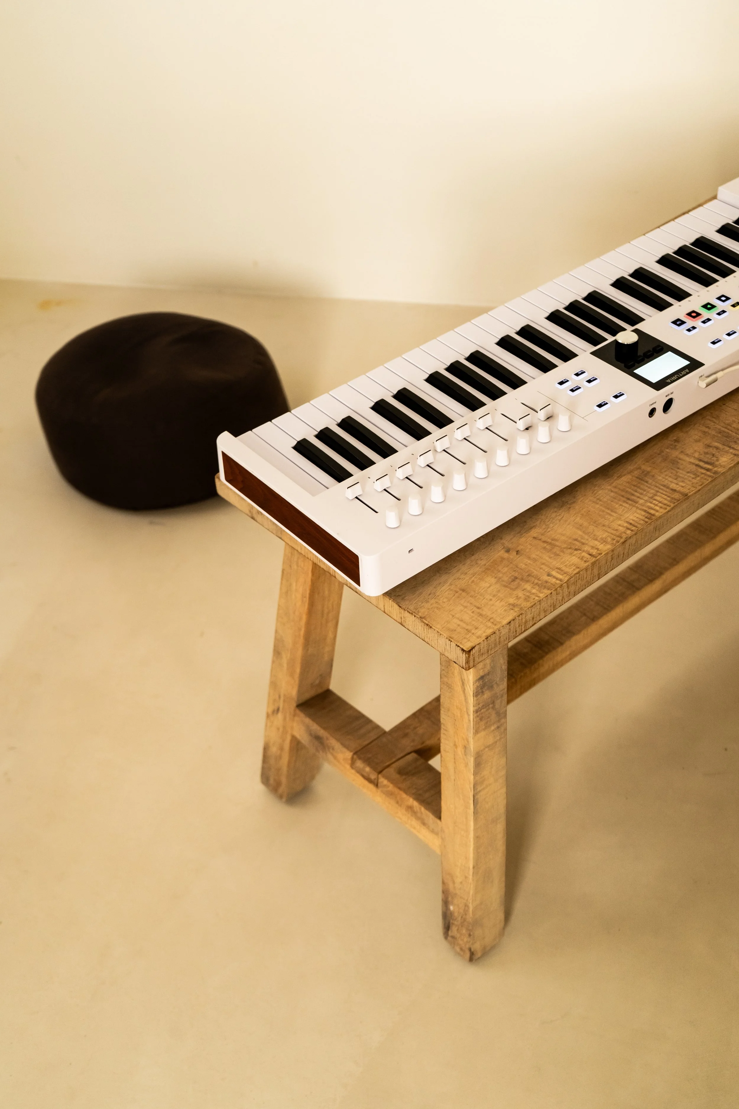Un teclado musical blanco y negro sobre una mesa de madera. A la izquierda hay un cojín oscuro.