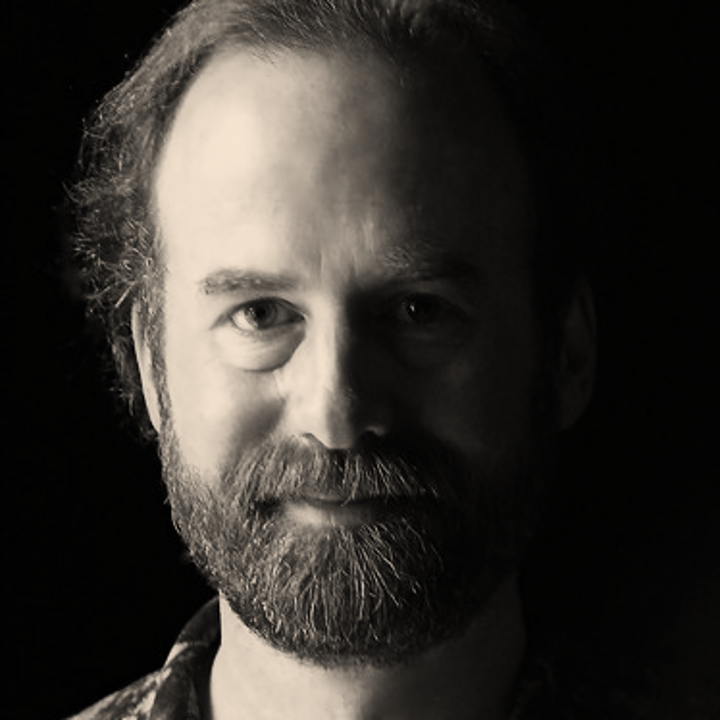 Black and white portrait of a man with a beard and mustache, looking directly at the camera with a subtle smile.