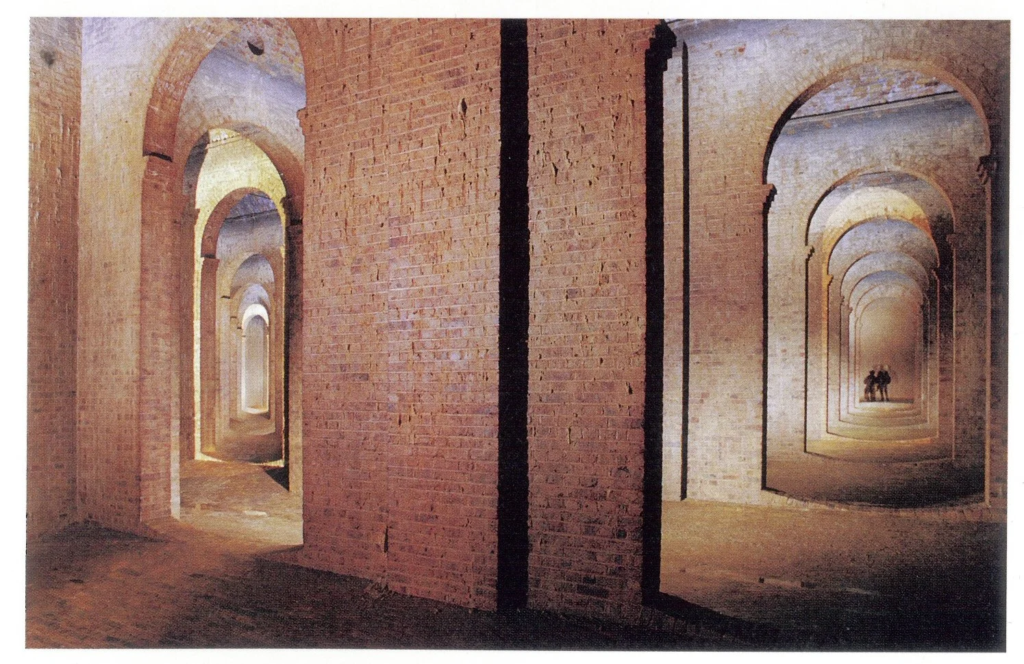 A series of brick archways with a view through the openings, leading to a distant figure of two people standing together. A drained Claremont Square reservoir, 2000.