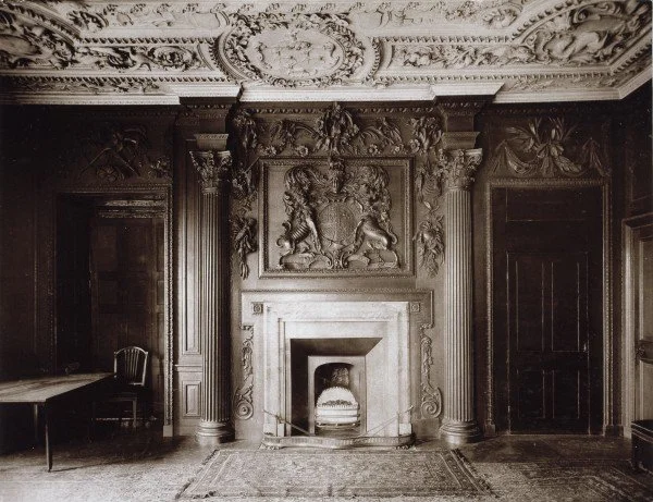 An ornate historical room featuring a large decorative fireplace with detailed carvings, flanked by two columns, and a carved lion crest above. The Oak Room within the old Metropolitan Water Board offices.