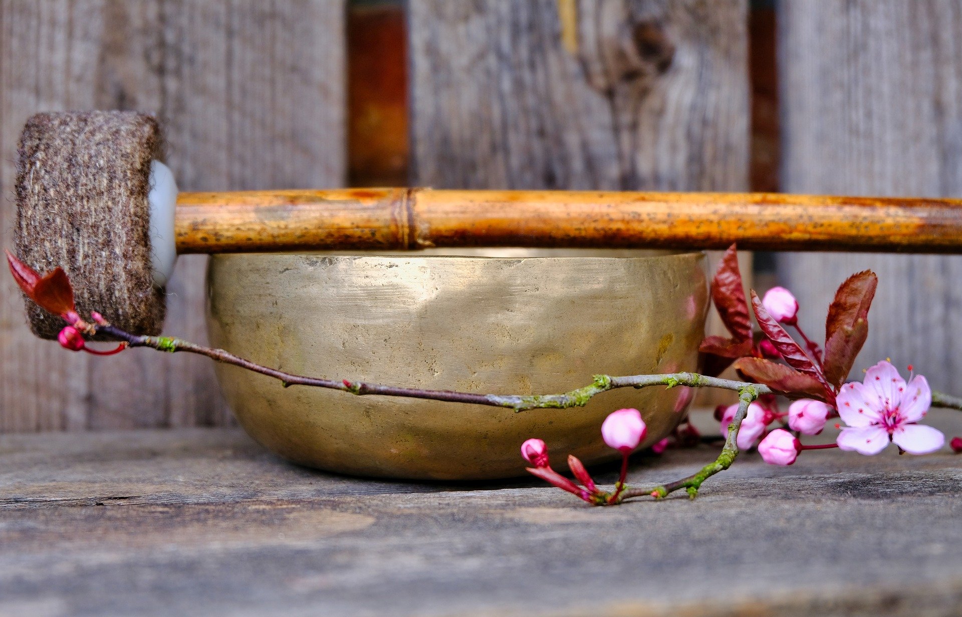 Eine Holzschale mit Sandsteinoptik, auf einem Holzbrett, dekoriert mit blühenden Zweigen und pinken Blumen, vor einem Holzhintergrund.