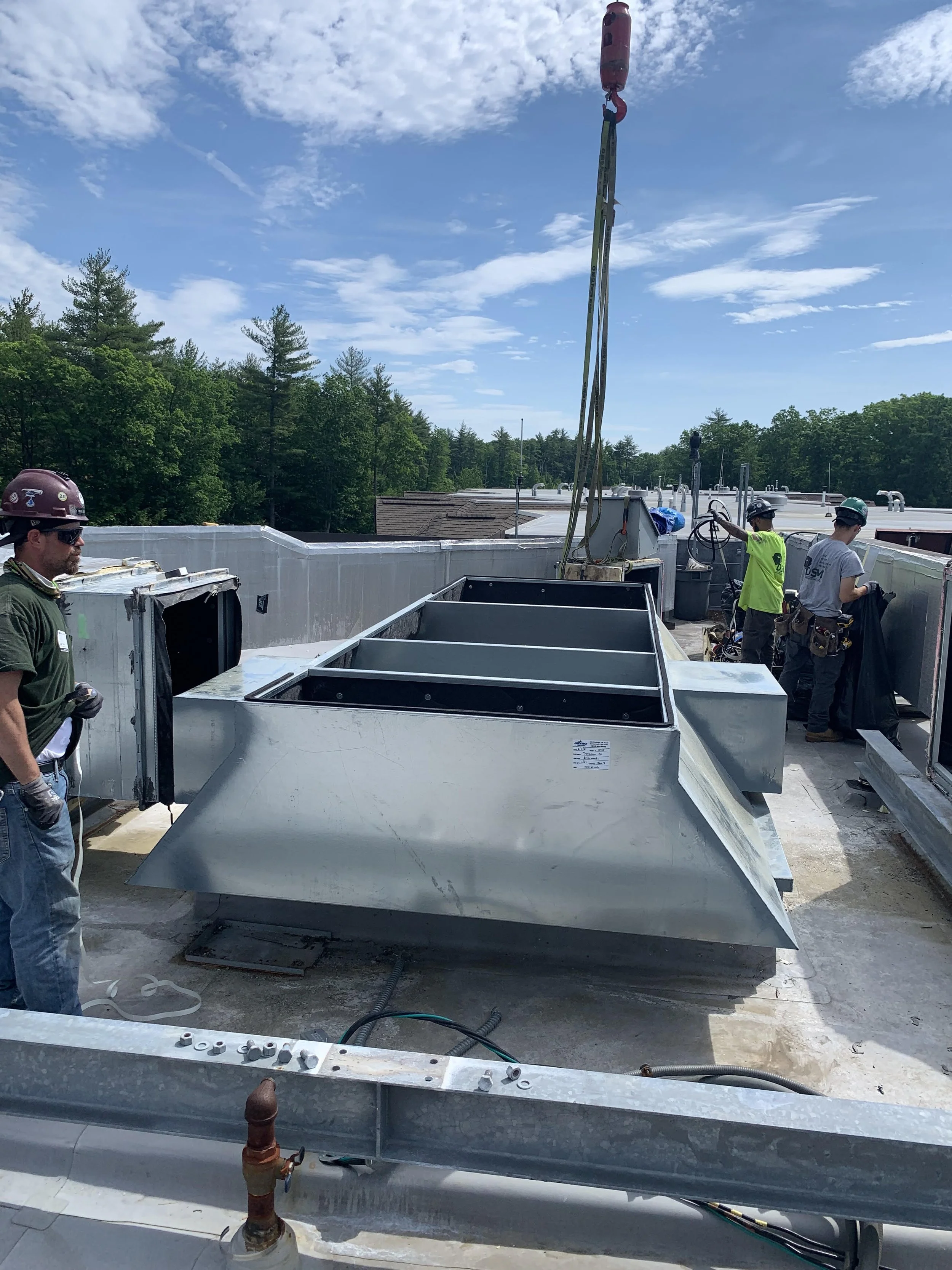 Workers installing HVAC units on a building rooftop during daytime with a blue sky and clouds in the background.