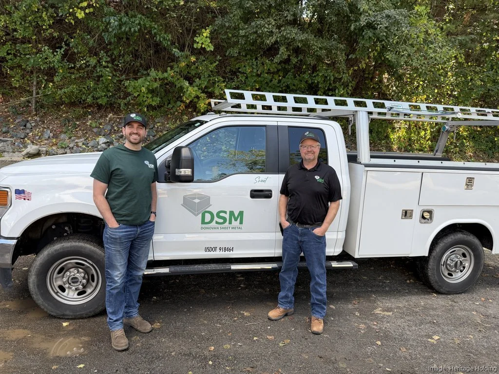 Two men standing in front of a white utility truck with the logo DSM Donovan Sheet Metal, parked outdoors with green shrubbery behind.